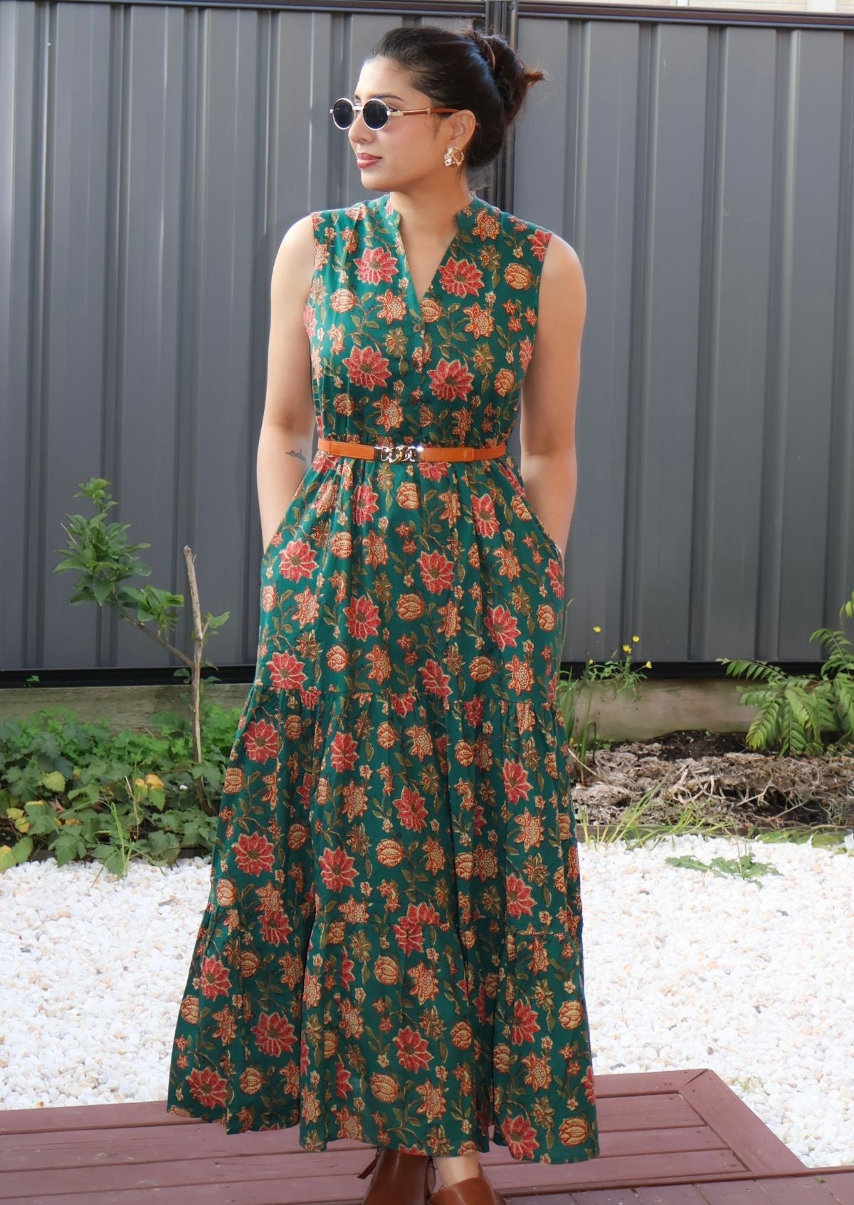 Woman wearing a cotton green floral dress standing outdoors with a gray wall and plants in the background.