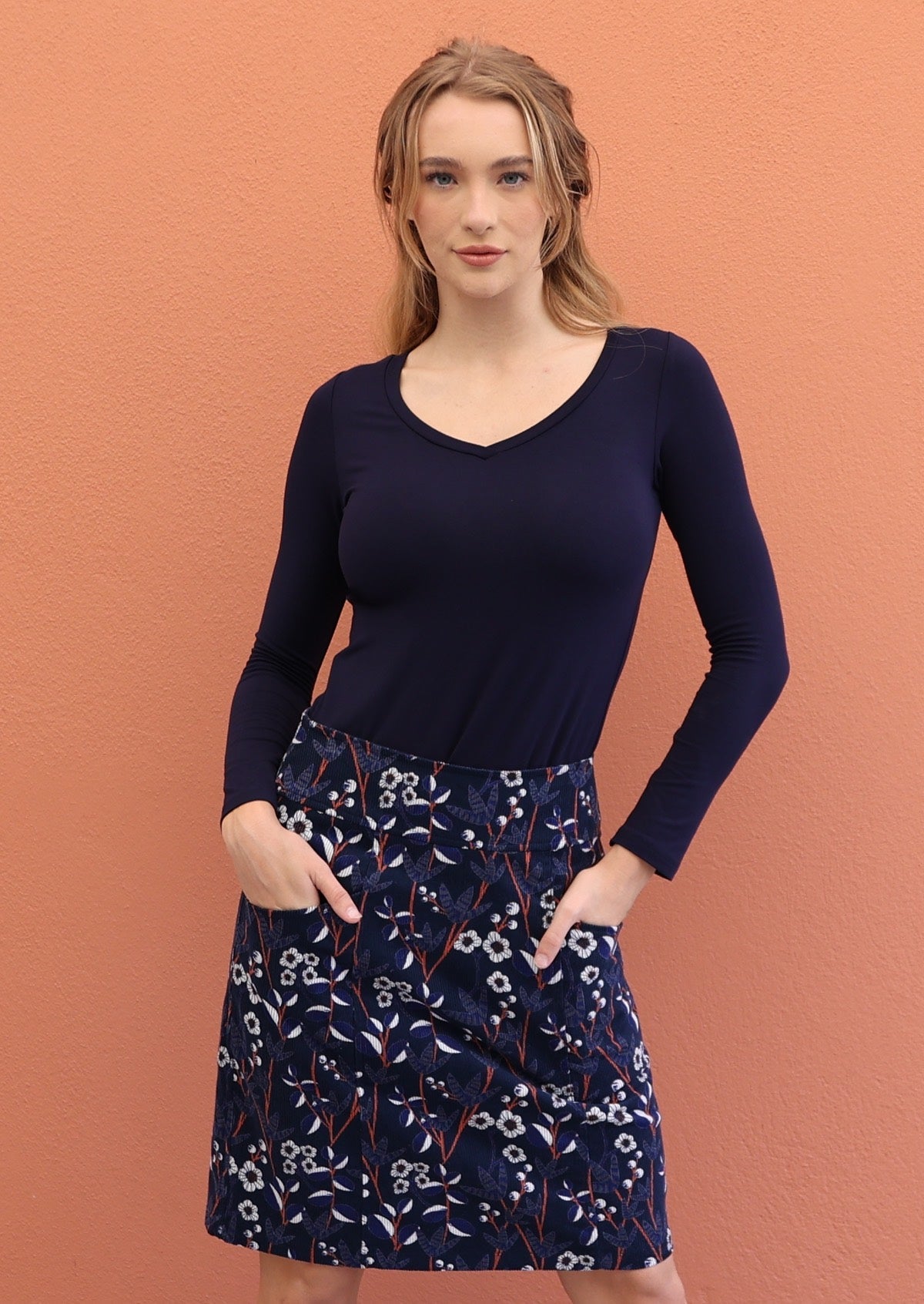 Model wears gorgeous floral print on navy blue based cotton corduroy skirt with both hands in pockets.