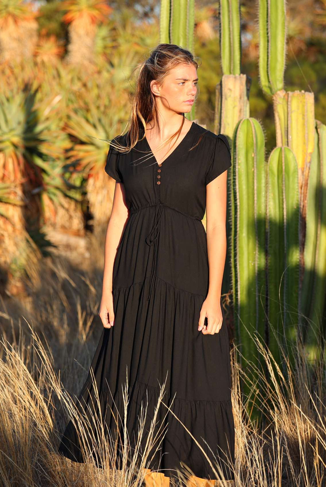 Woman wears black rayon maxi dress with voluminous tiered skirt and buttoned bodice
