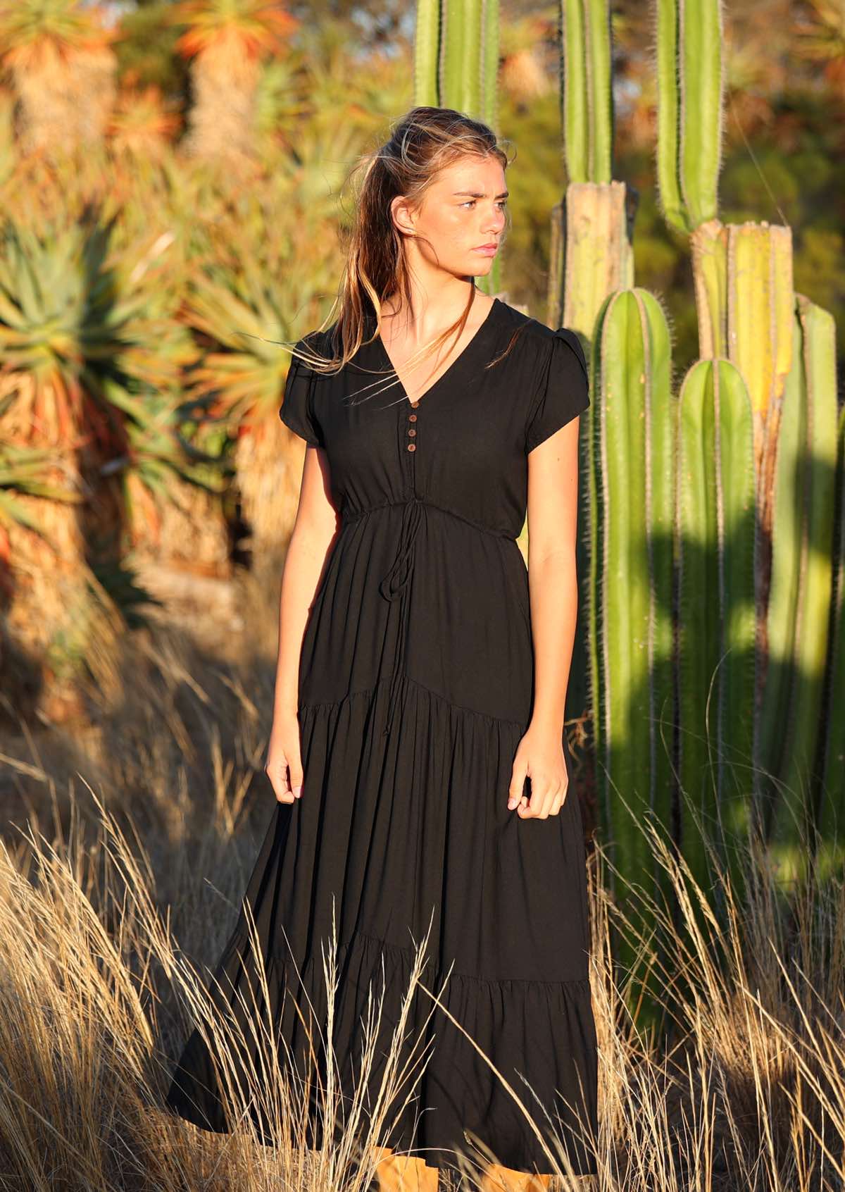 Woman wears black rayon maxi dress with voluminous tiered skirt and buttoned bodice