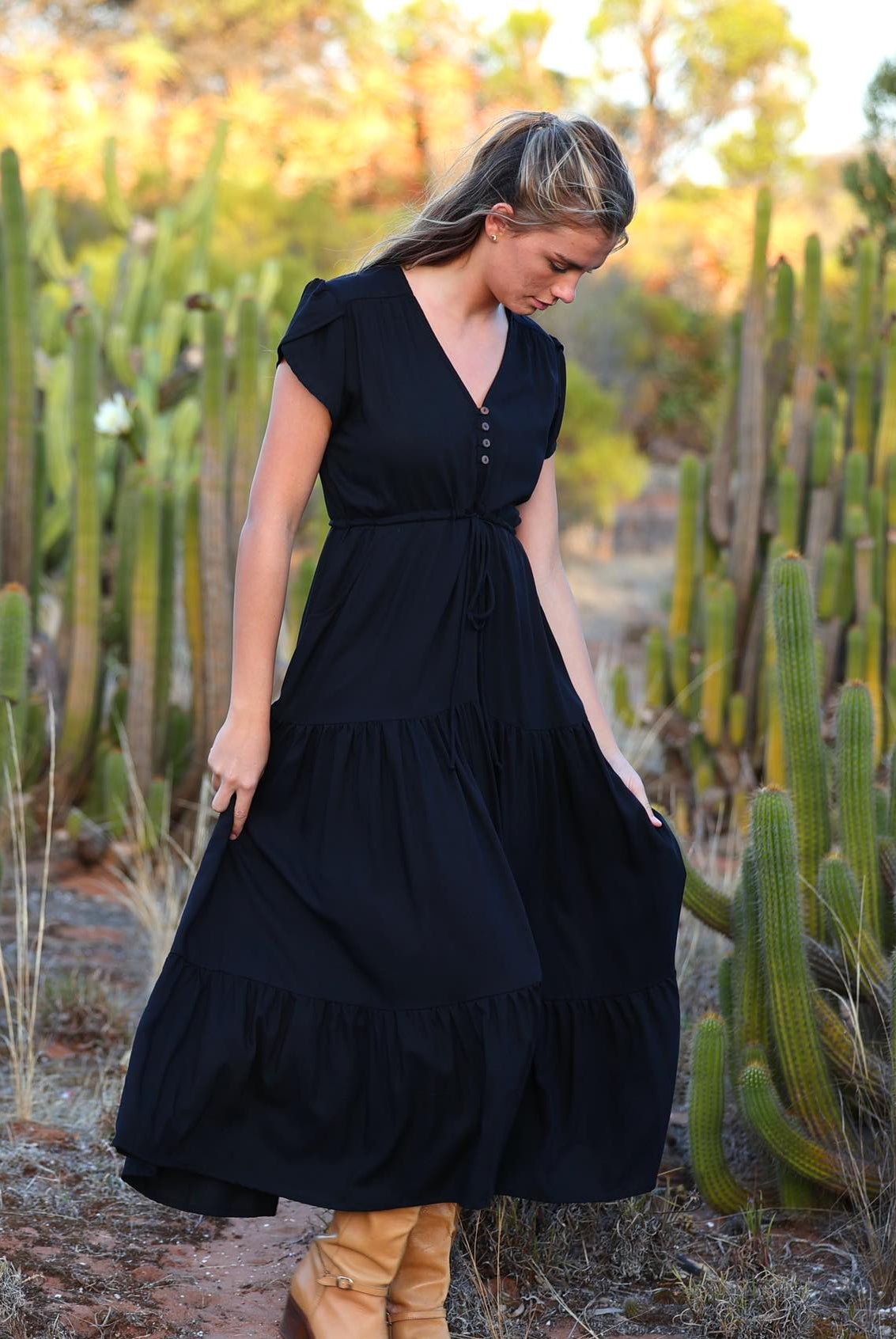 Woman stands in black rayon maxi dress with V-neckline and buttoned bodice and hidden side pockets