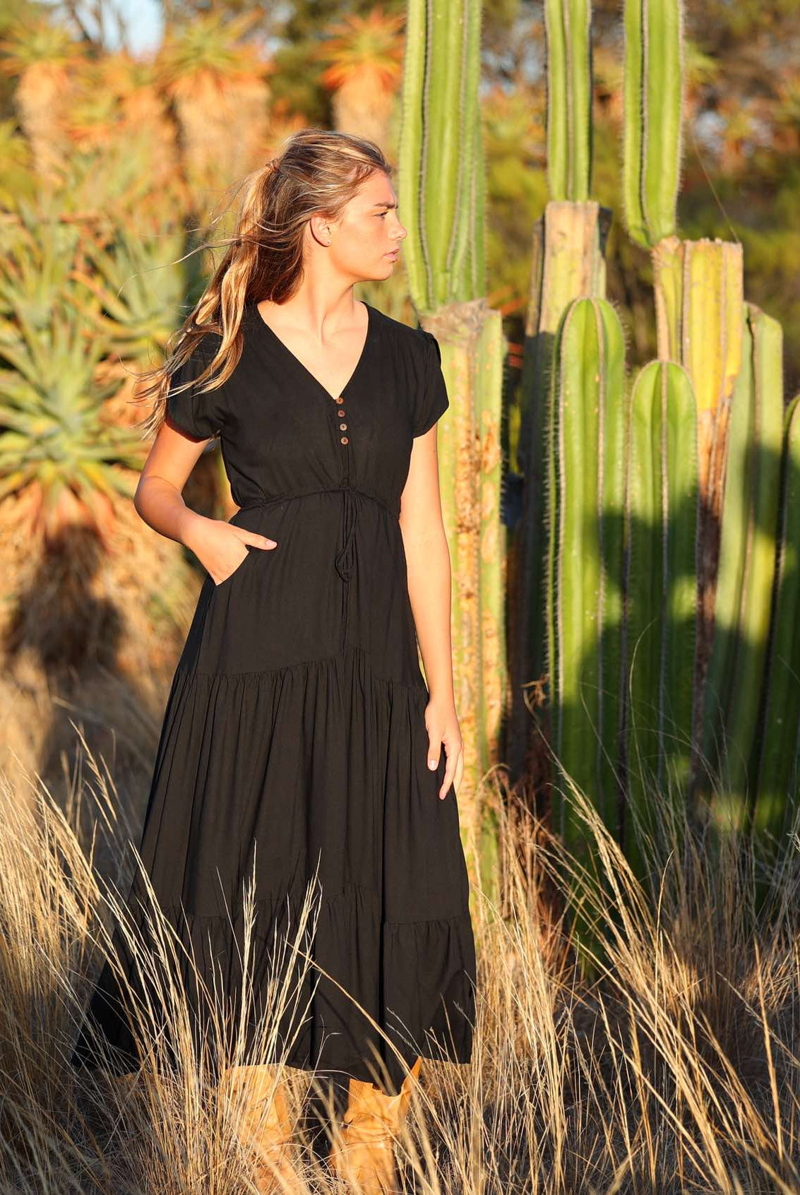 Woman poses in black rayon maxi dress with V-neckline, buttoned bodice, waist-tie and pockets