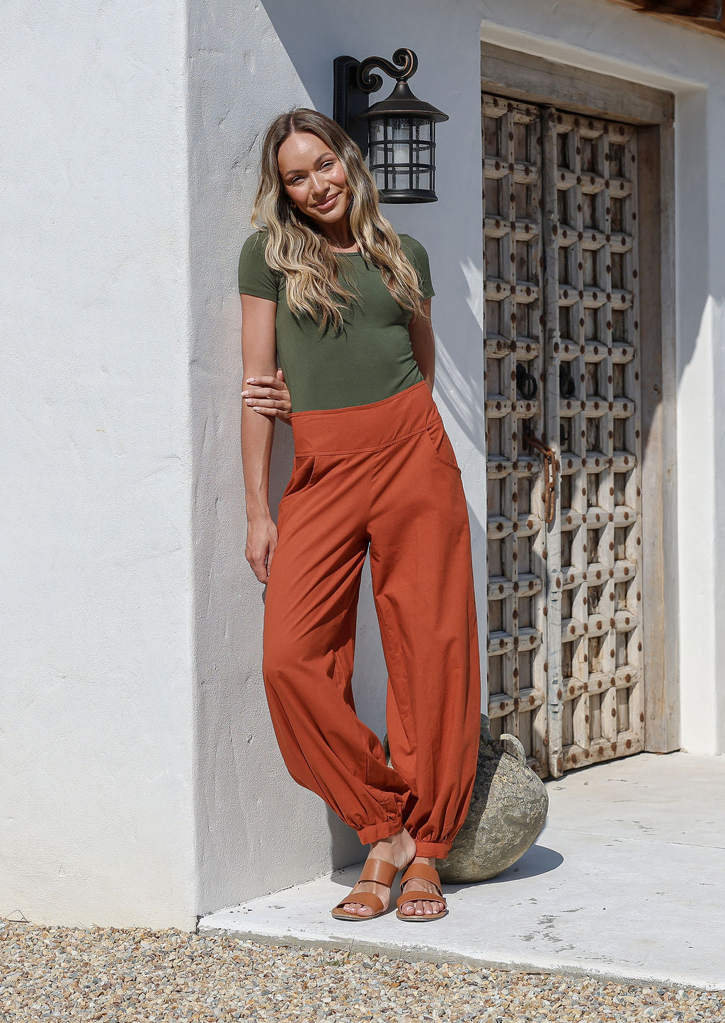 Woman standing in sun wearing a 100% cotton rustic orange wide leg pants with pockets, cuffed ankles and wide flat front waistband
