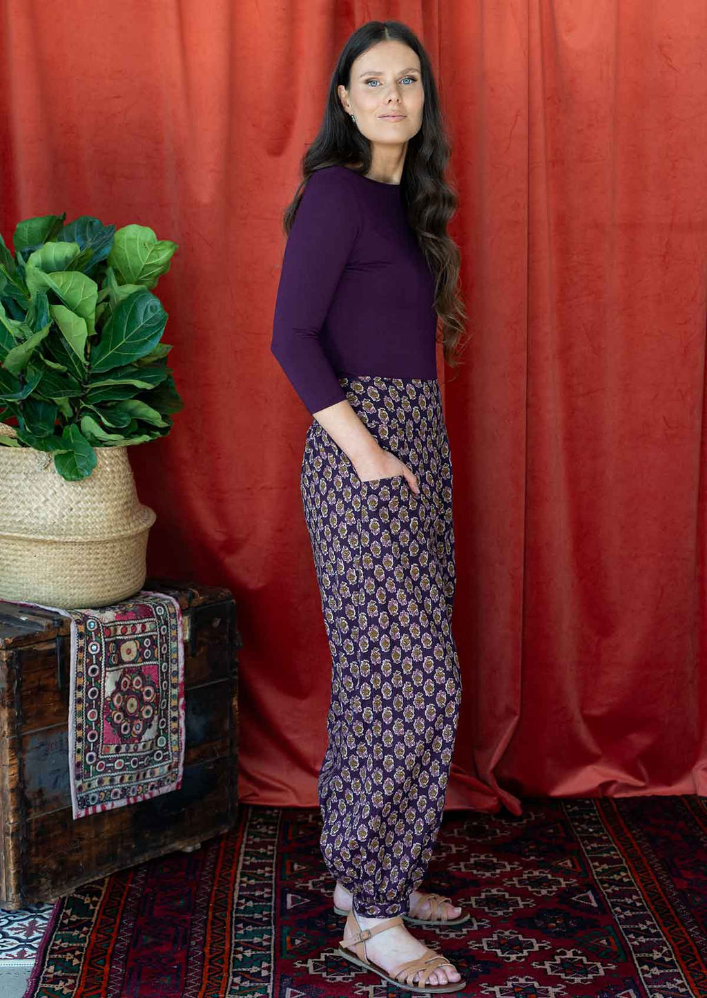 Woman wears cotton harem pants with buttoned ankle and pockets, paired with a dark purple top