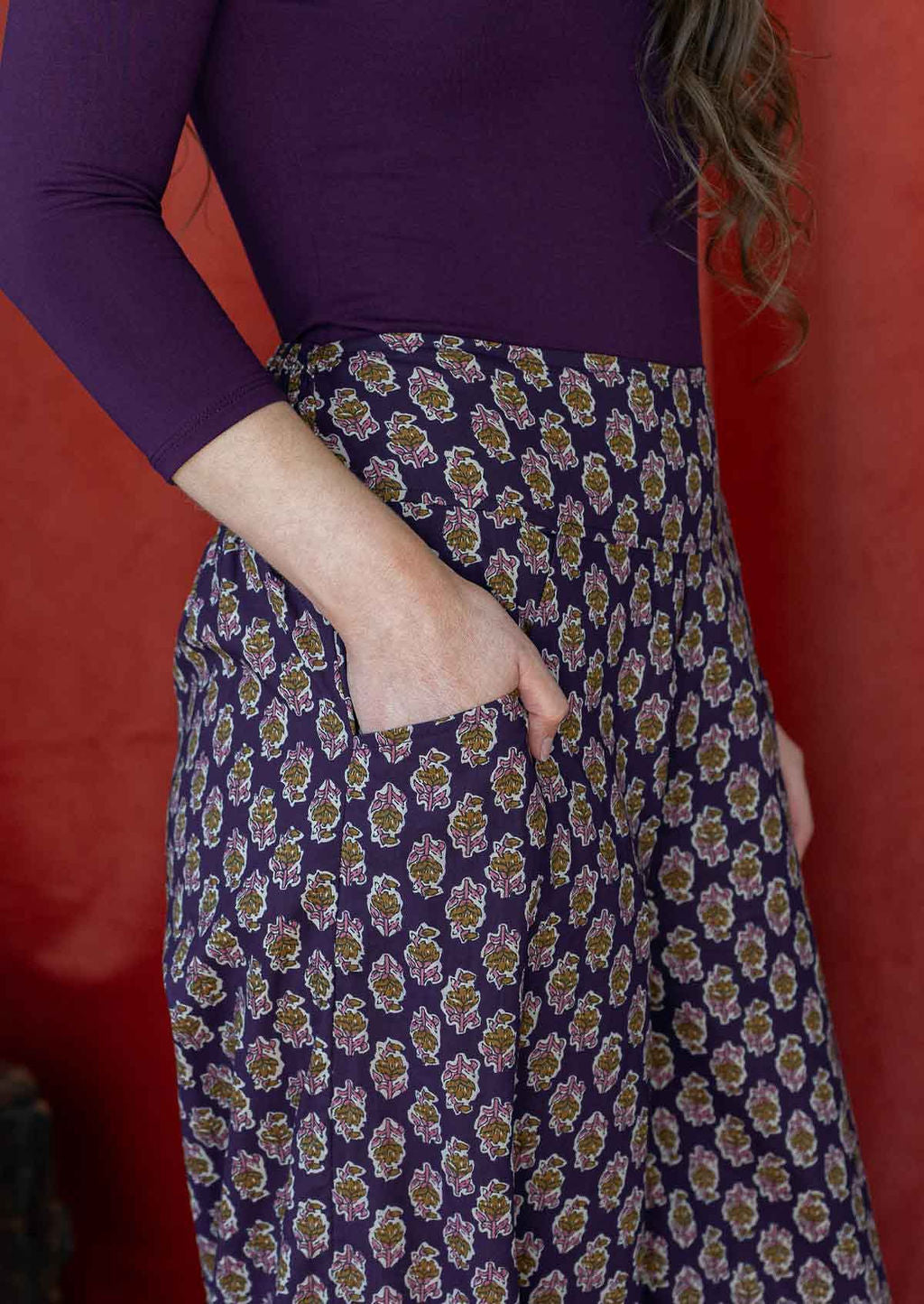 Close up of floral motif print on a purple base cotton pants, with model's hand in pocket