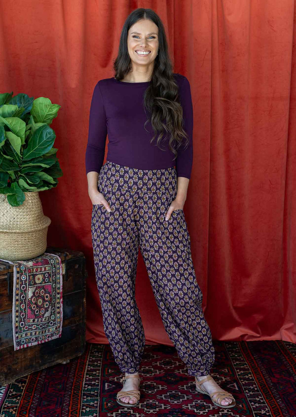 Model poses in cotton harem pants with buttoned ankle and pockets, paired with a dark purple top