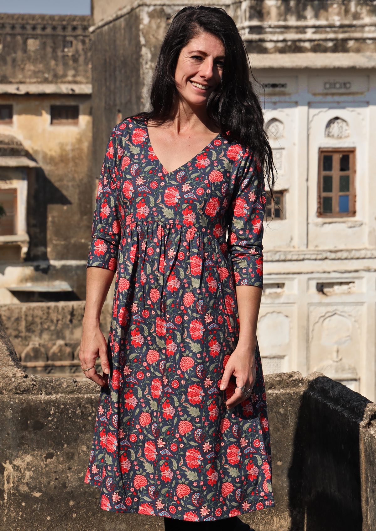 Woman wears relaxed fit cotton 3/4 sleeve V-neckline dress with small gathers at empire waistline