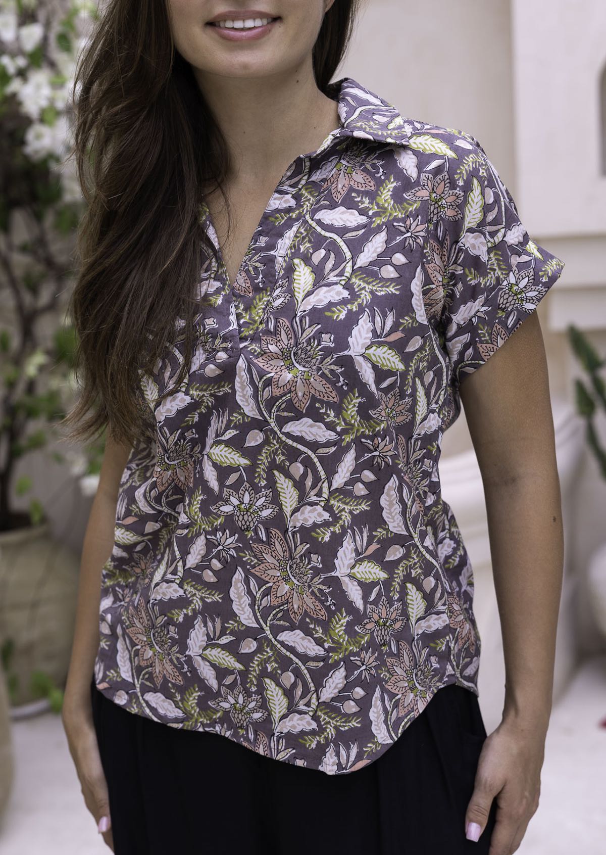 Model wears short sleeve relaxed fit cotton top with V-neckline and collar, in coral pink, lime green and beige florals on taupe base.
