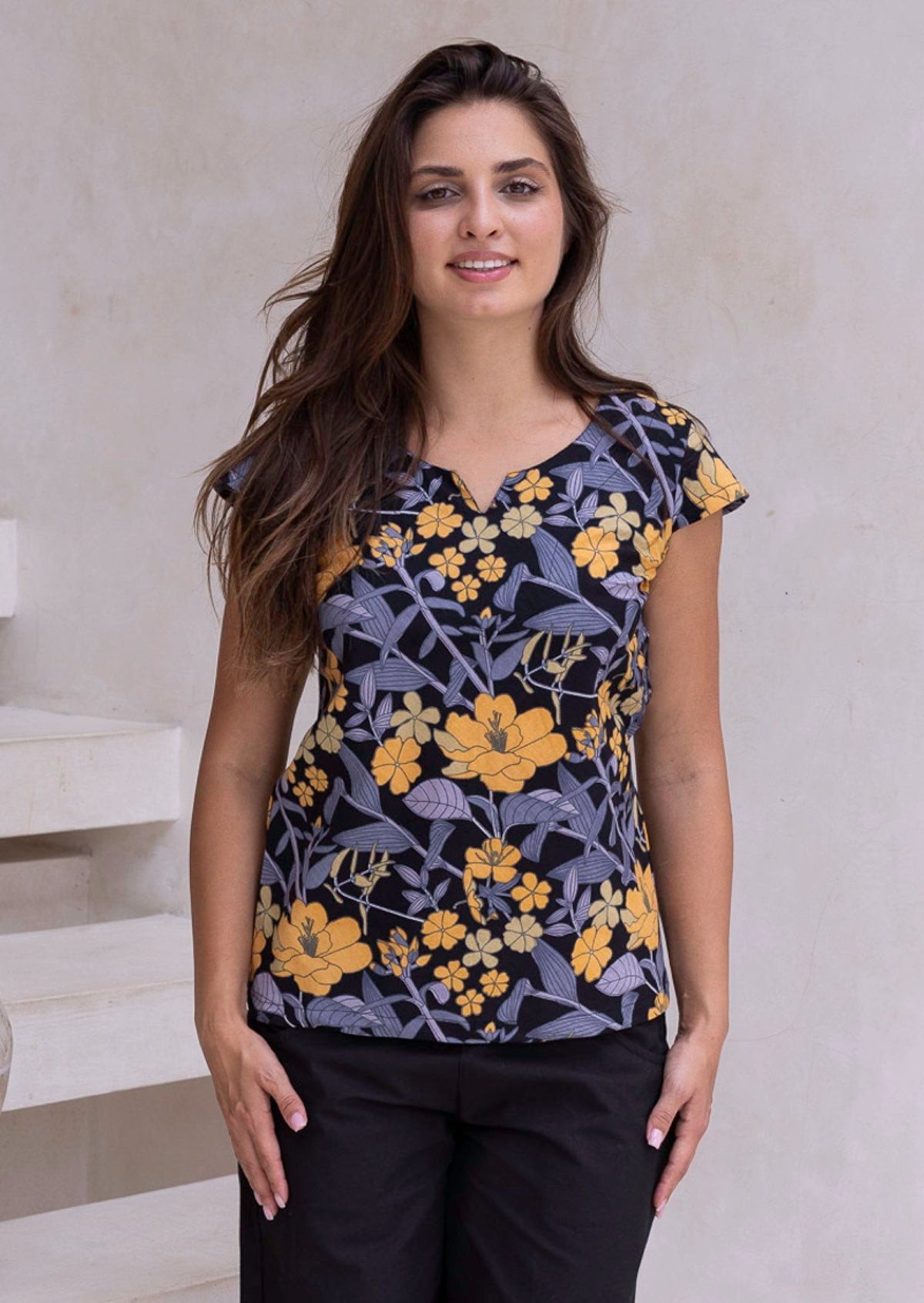 Woman standing in a 100 percent cotton floral print top with cap sleeves, round neckline and keyhole cutout.
