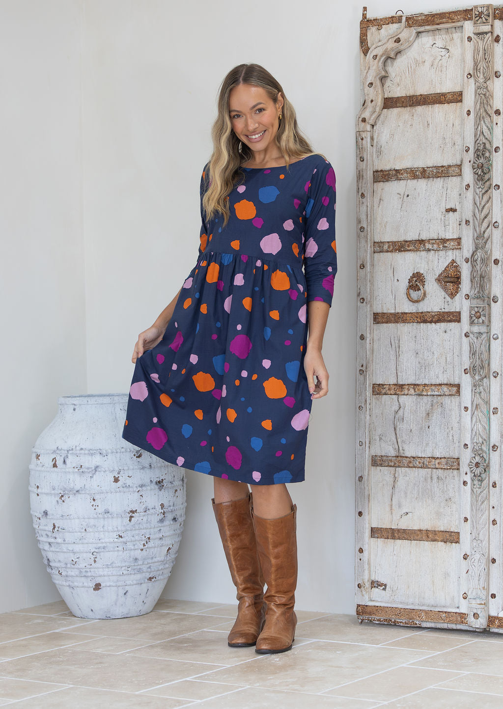 Woman wearing a polka dot dress with 3/4 sleeves and a boat neckline, paired with tan boots