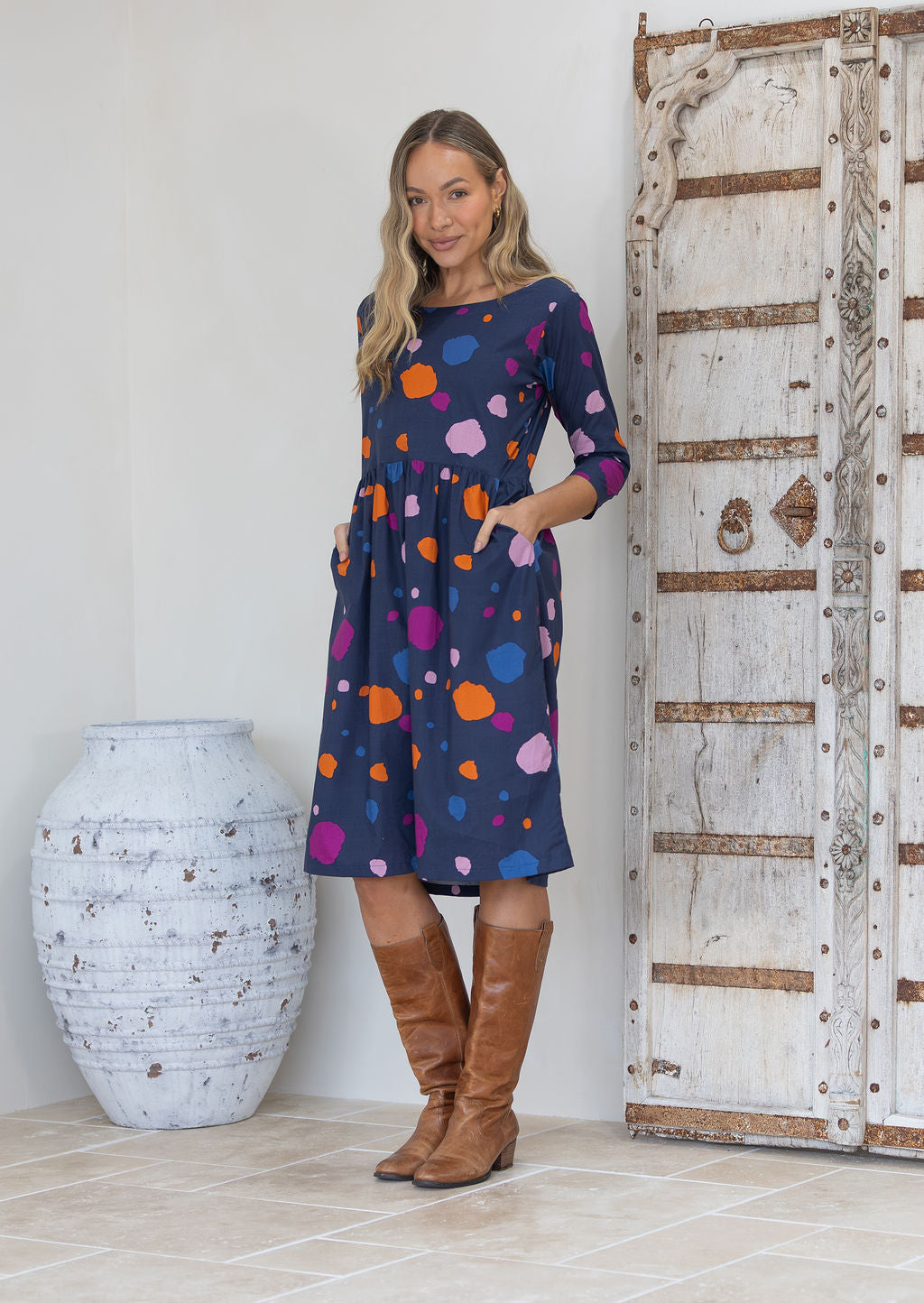 Woman wearing a cotton dress with colourful polka dots on a blue base with hands in pockets