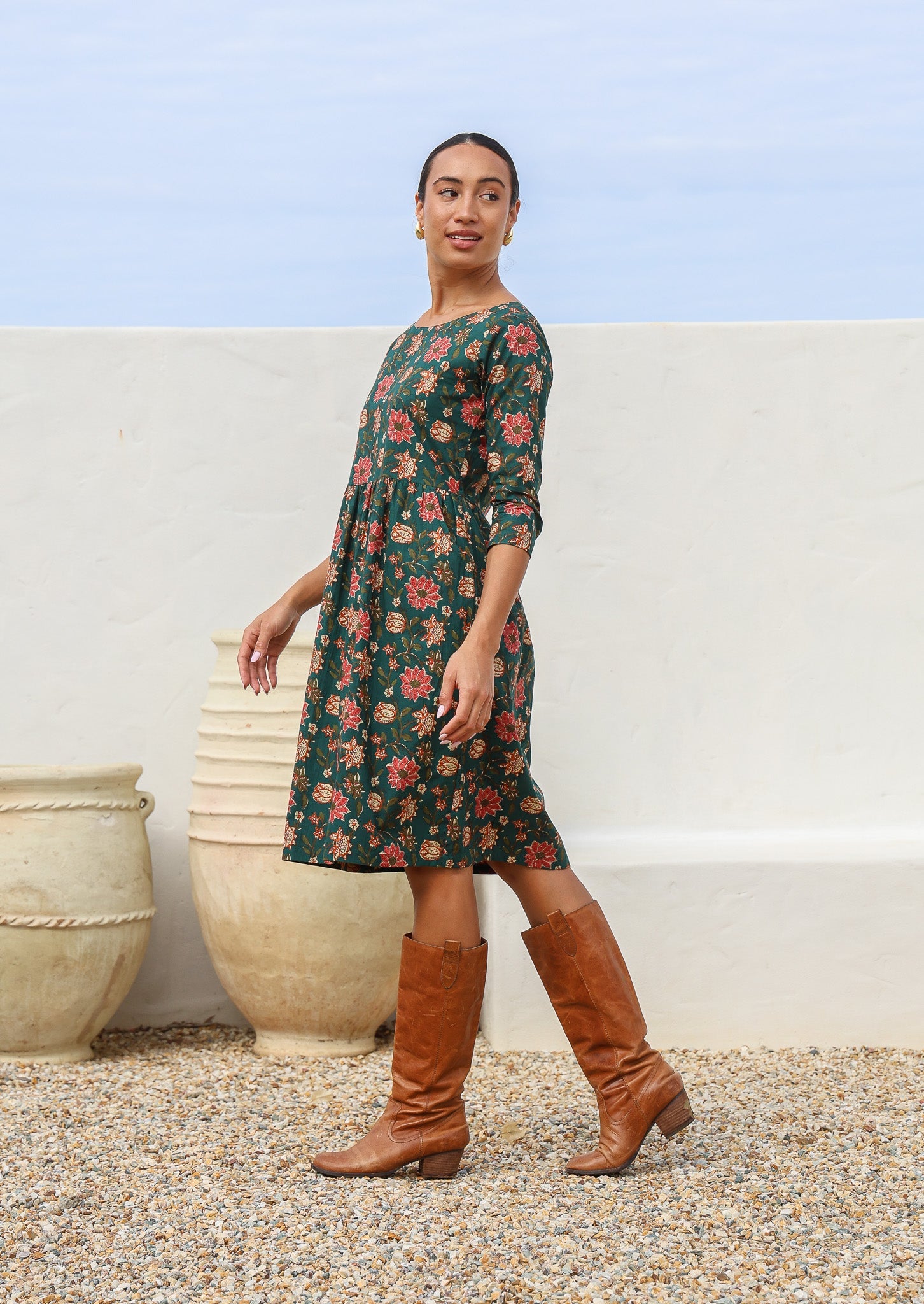 Woman standing sideways wears midlength, floral print cotton dress with 3/4 sleeves and small gathers at loose waist.