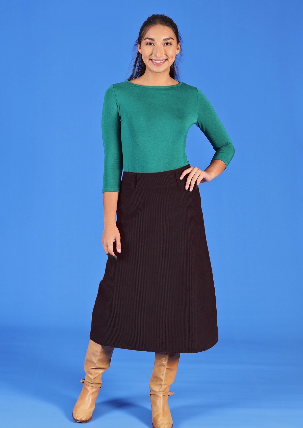 Woman wearing a-line below knee length black corduroy skirt with green long sleeve top