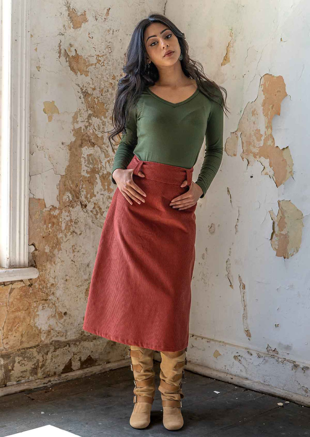 Woman with dark hair wears an olive long sleeve rayon top with a midi length corduroy skirt in burnt henna
