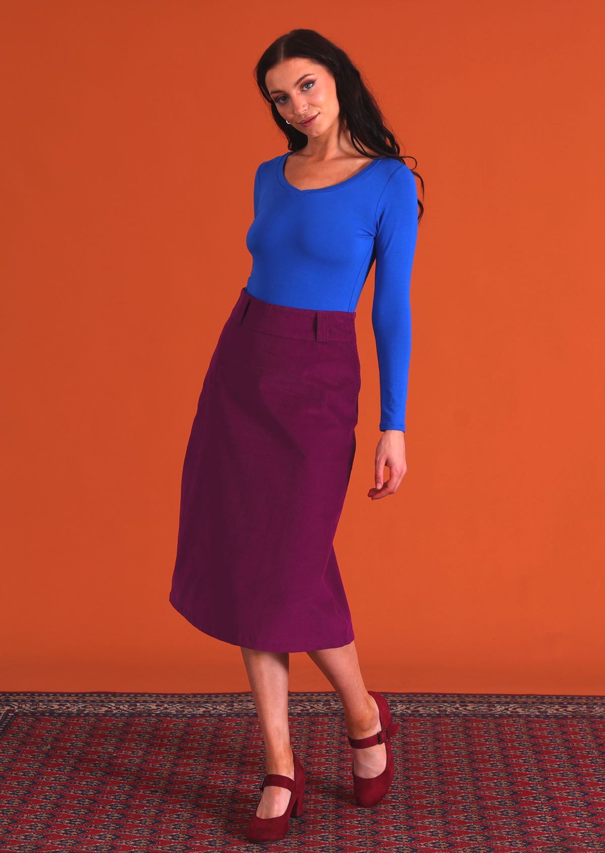 woman wearing purple corduroy aline skirt with belt loops with bright blue v-neck long sleeve top