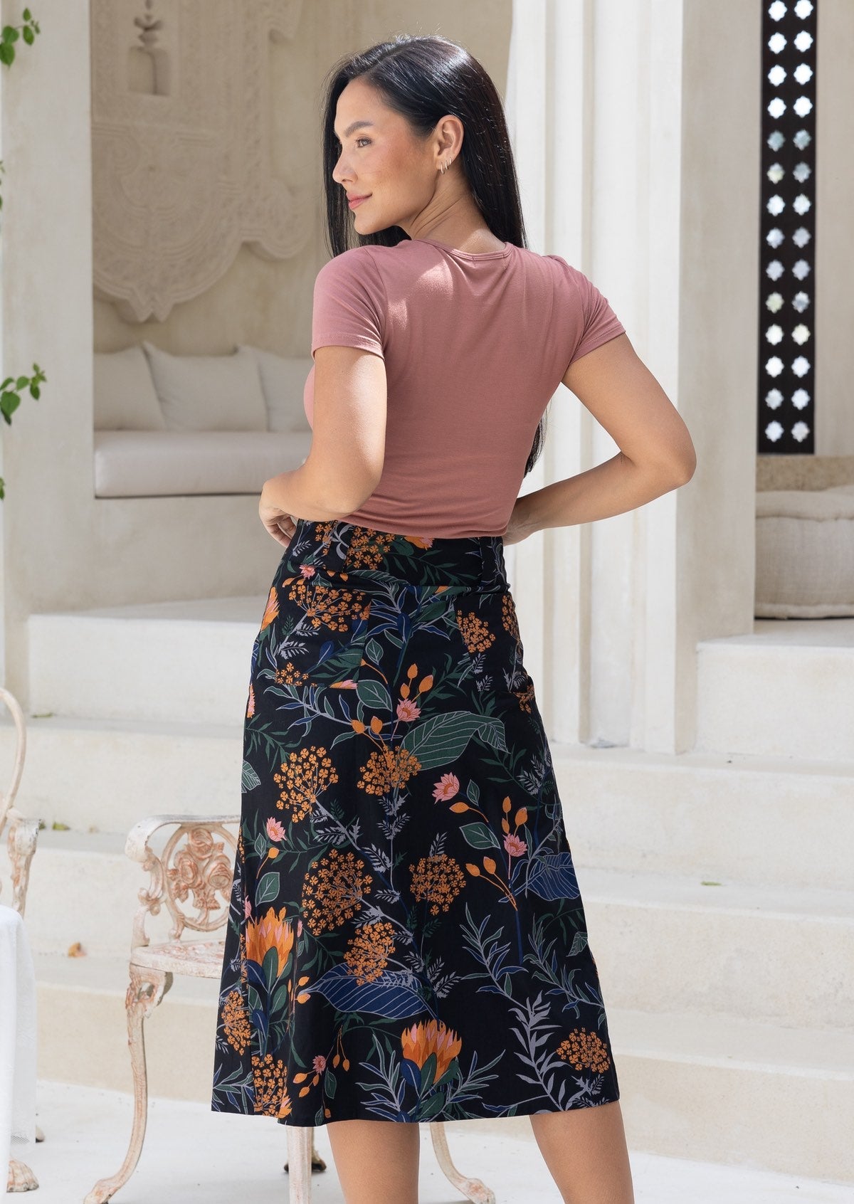 Back view of a woman in a dark blased cotton midi length skirt with two back pockets and belt loops