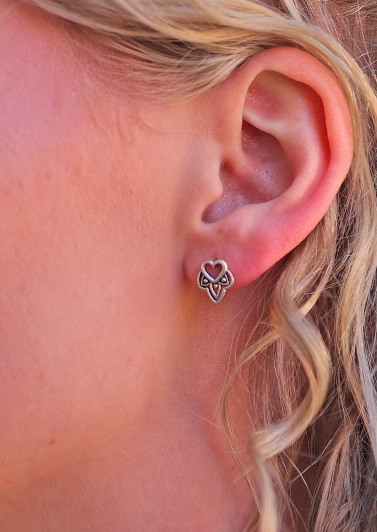 A close-up image of a woman's ear wearing a silver Boho heart-shaped stud earring with a tribal design at the base.