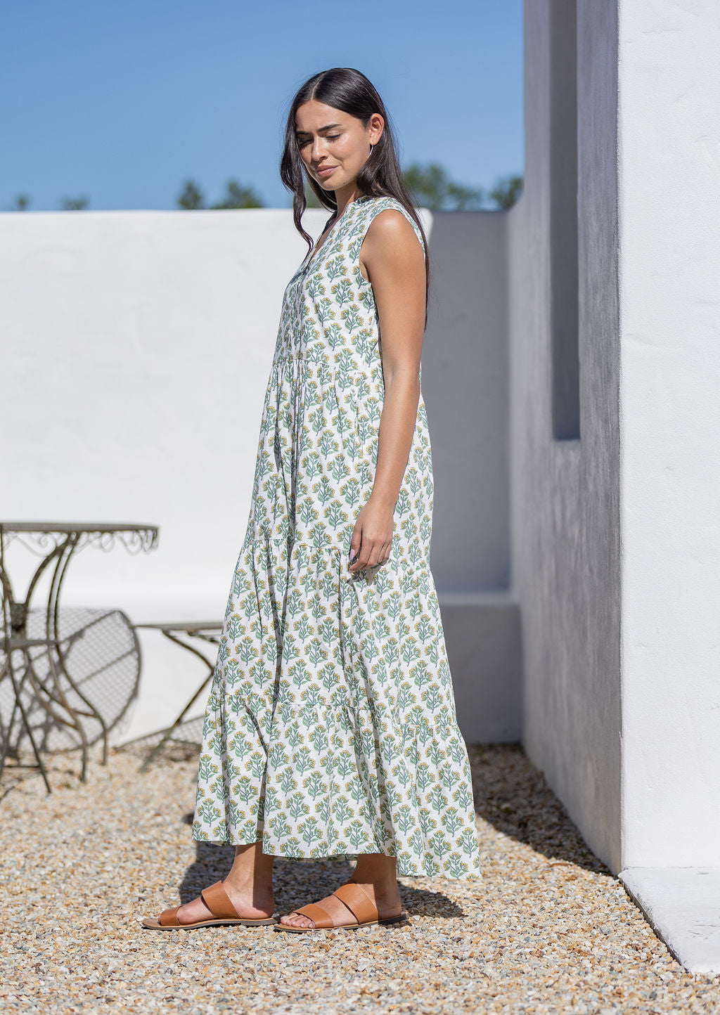 Woman wearing a long white floral cotton dress standing outdoors near a white wall.