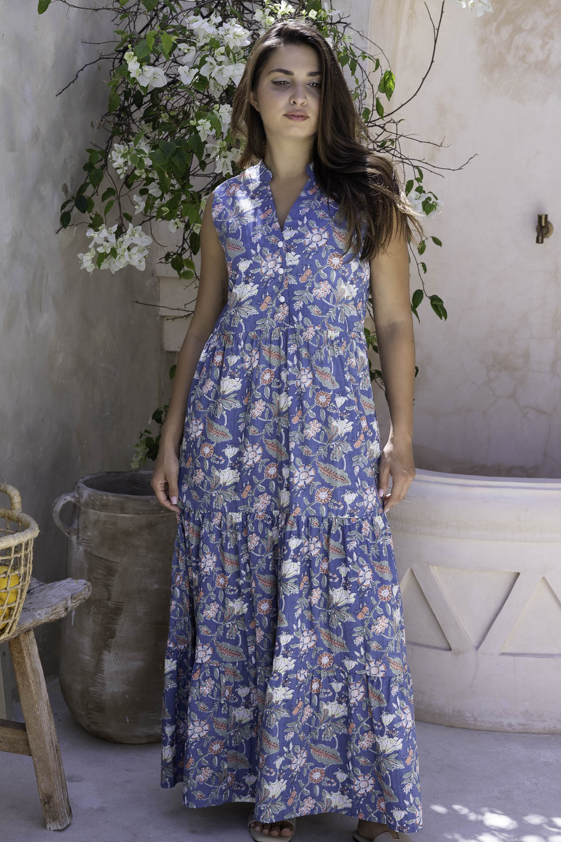 Woman wearing a sleeveless cotton maxi dress with buttoned bodice, 3 tiered maxi skirt, mandarin collar in dusty blue based floral print.