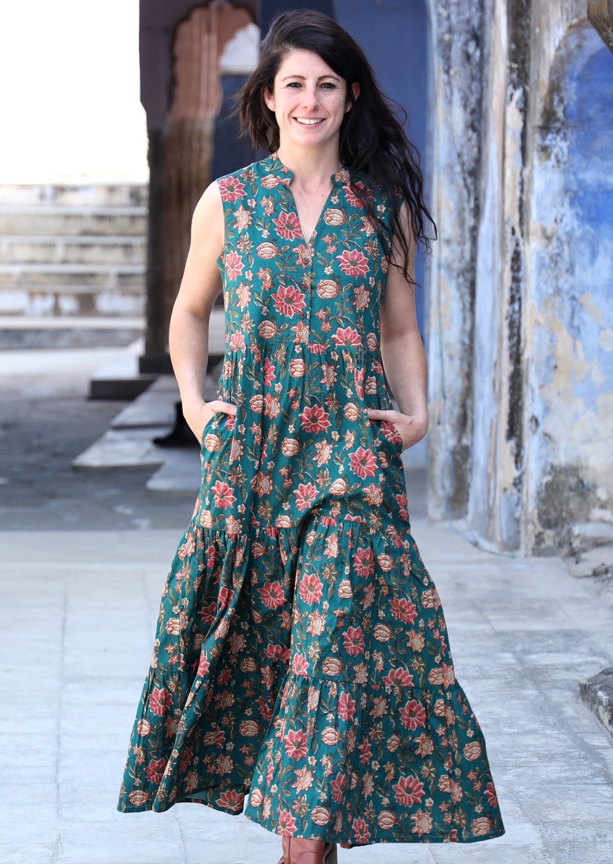 Model flaunting a beautiful floral printed 3 tiered maxi dress with hands in pockets and without sleeves.