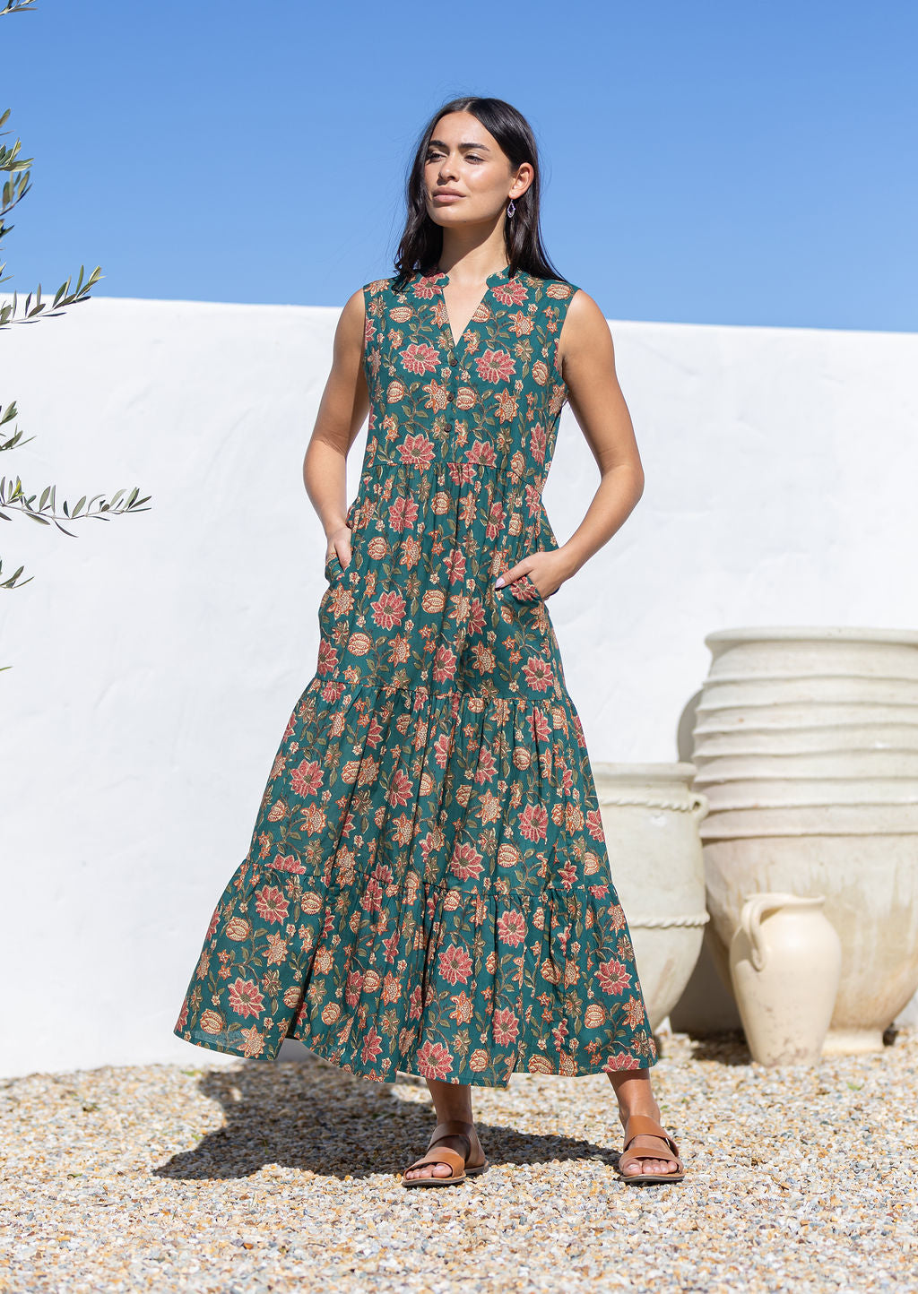 Woman wearing a green floral cotton dress standing outdoors with a white wall and potted plants in the background.