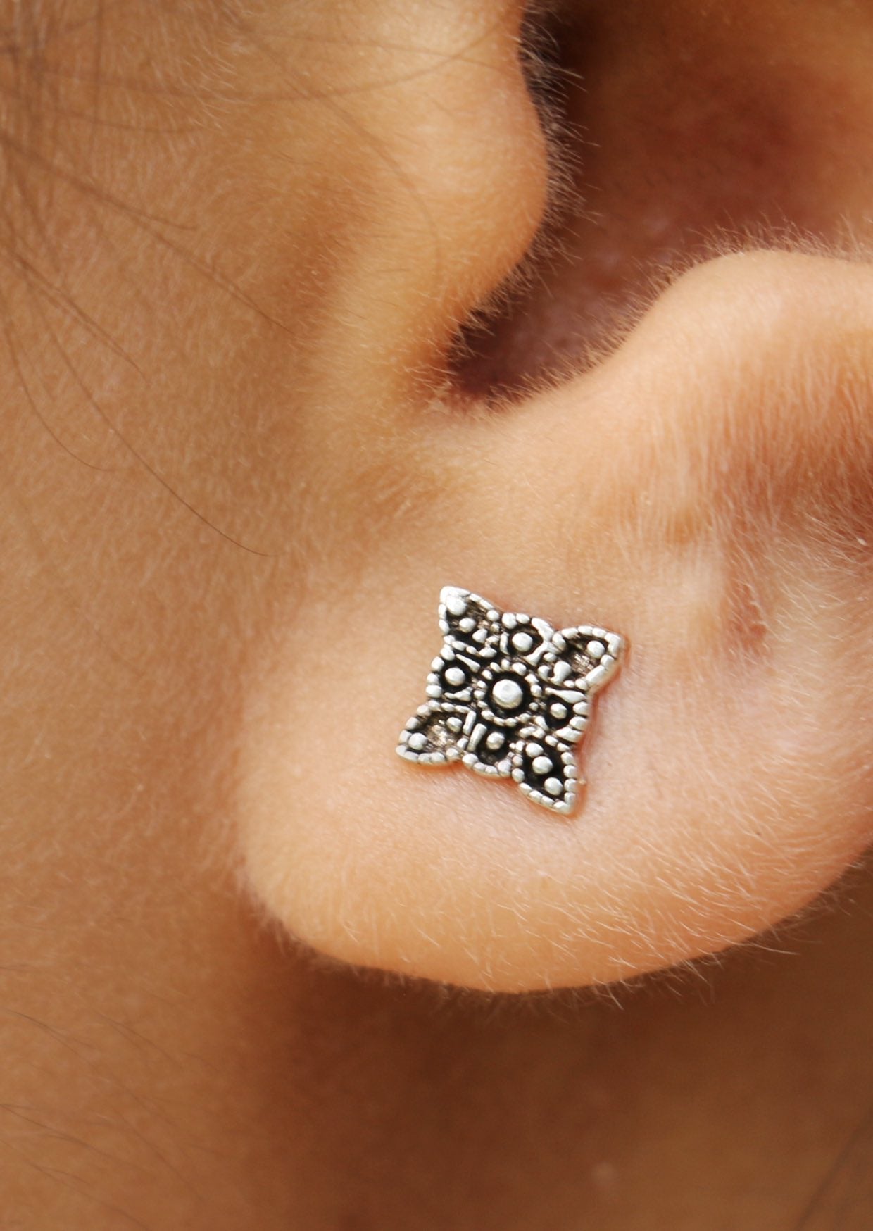 Close up of Boho Blooms silver studs featuring a delicate floral design, displayed on a woman’s ear