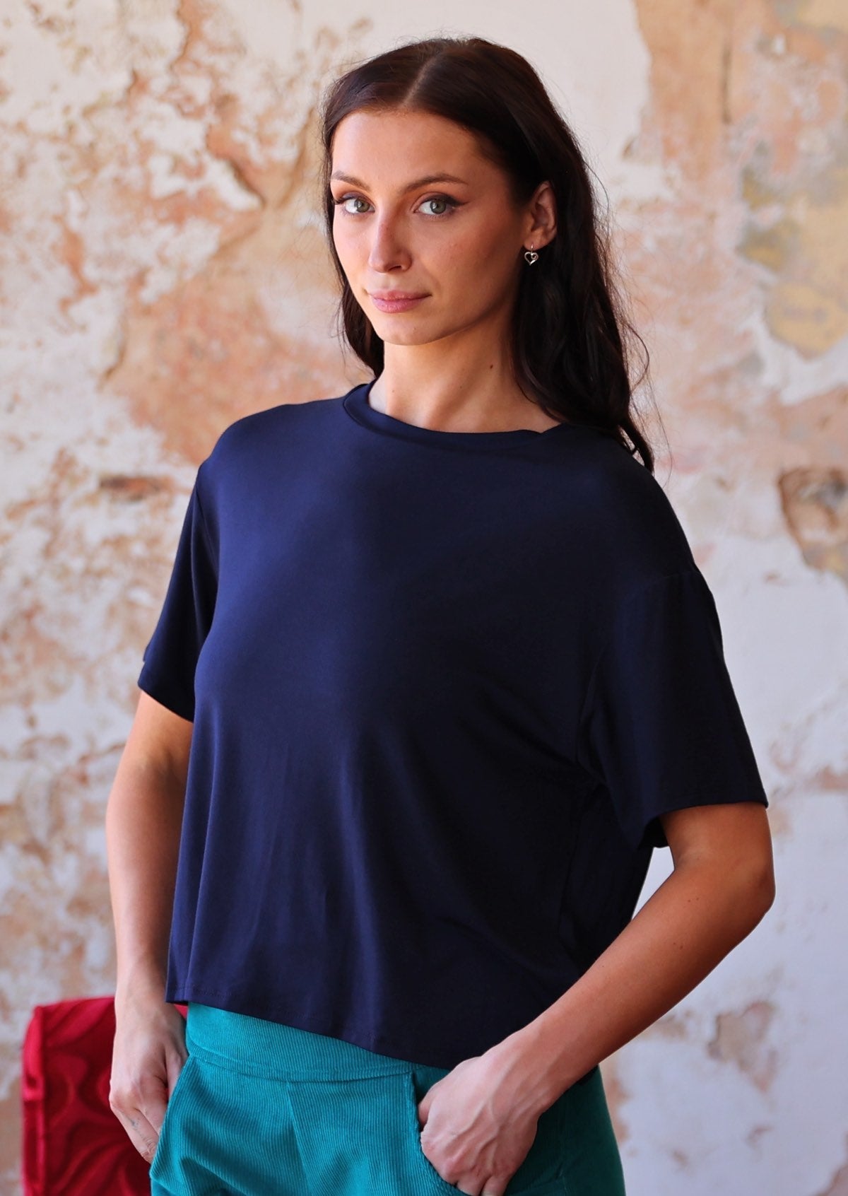 woman in navy blue rayon loose fit t-shirt over teal corduroy pants with hands in pockets