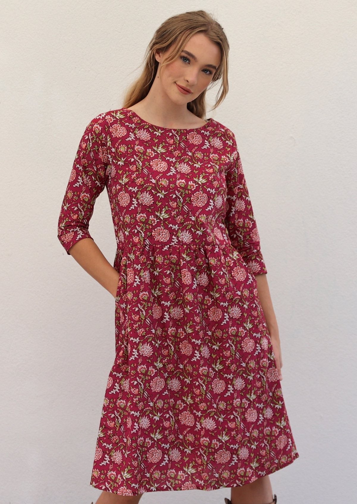 Model is wearing 100% cotton dress in sweet red cranberry base with pink florals, 3/4 sleeves and pockets.