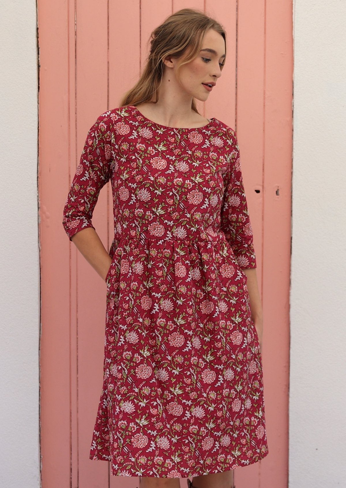 Model wears beautiful red cotton dress with wide round neckline and hand in a pocket.