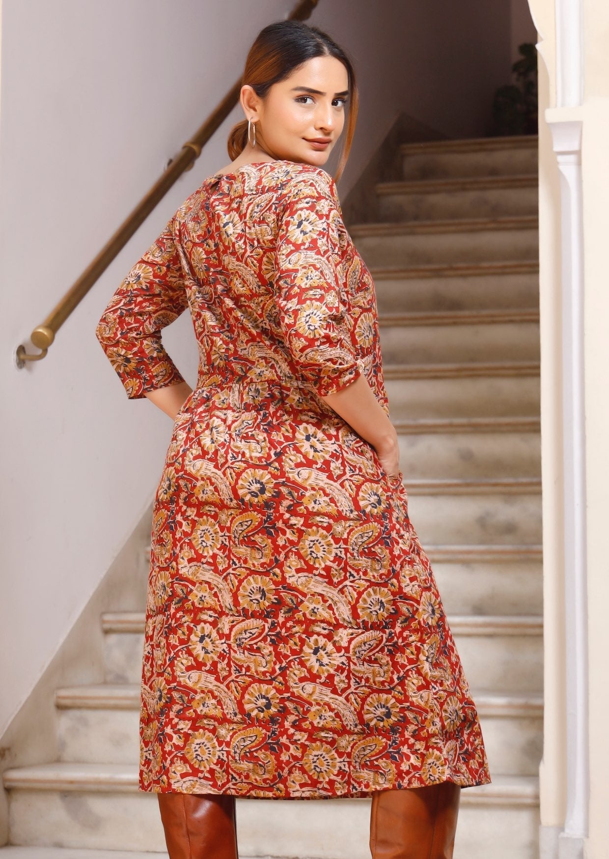 Back image of model with hands in pockets of red based floral print dress featuring button closure back