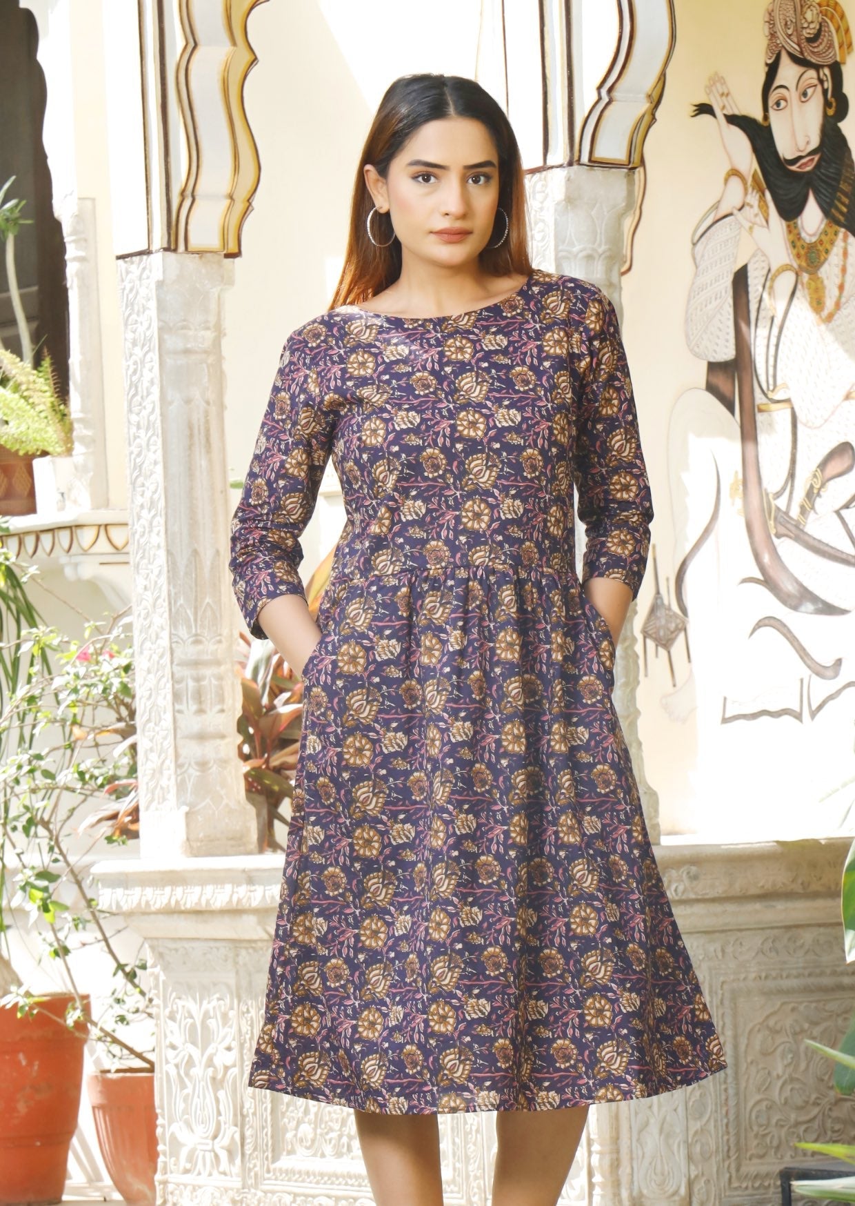 Model wears purple knee length cotton dress with 3/4 sleeves, round neckline and hands in pocket.