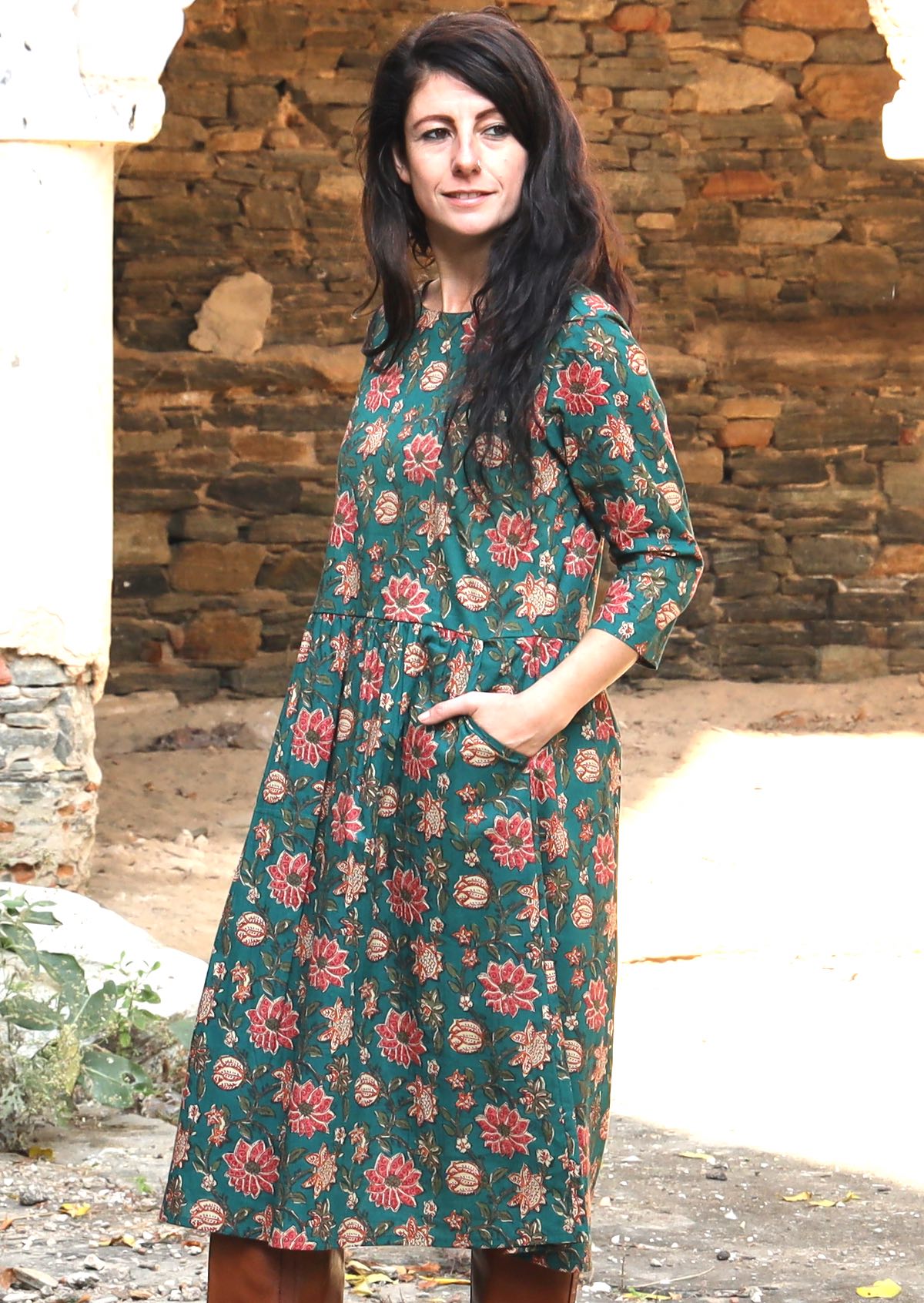 Model standing sideways wearing a deep green based cotton dress with beautiful floral print, 3/4sleeves and lining.