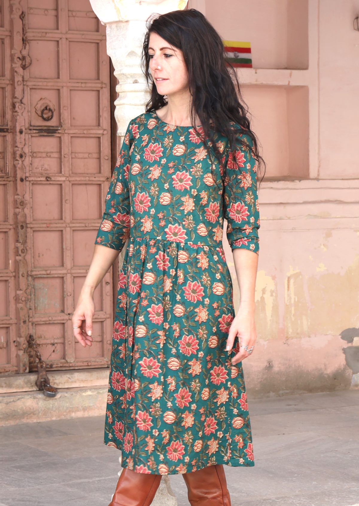 Model standing slightly Sideways wearing a beautiful green based floral printed cotton dress with pockets.