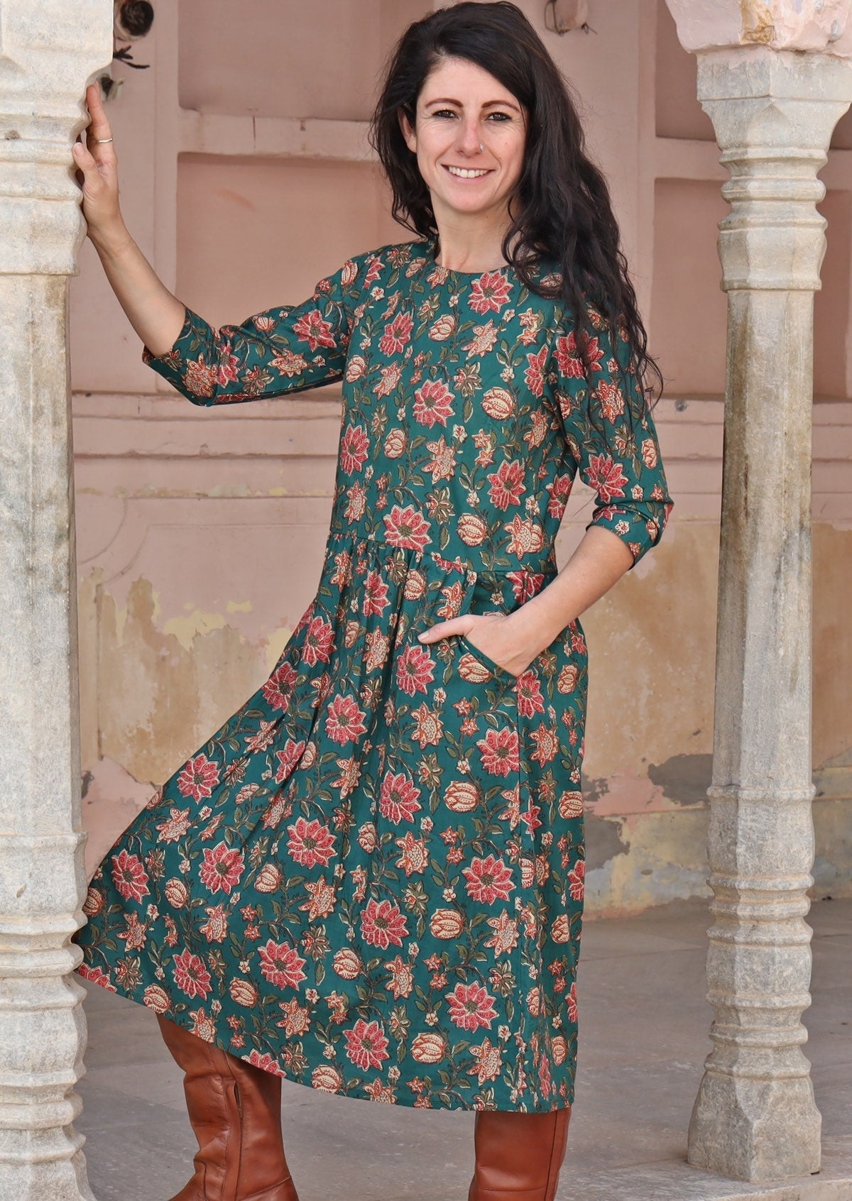 Model wearing 3/4 sleeves deep green based cotton dress with wide round neckline and one hand in pocket.