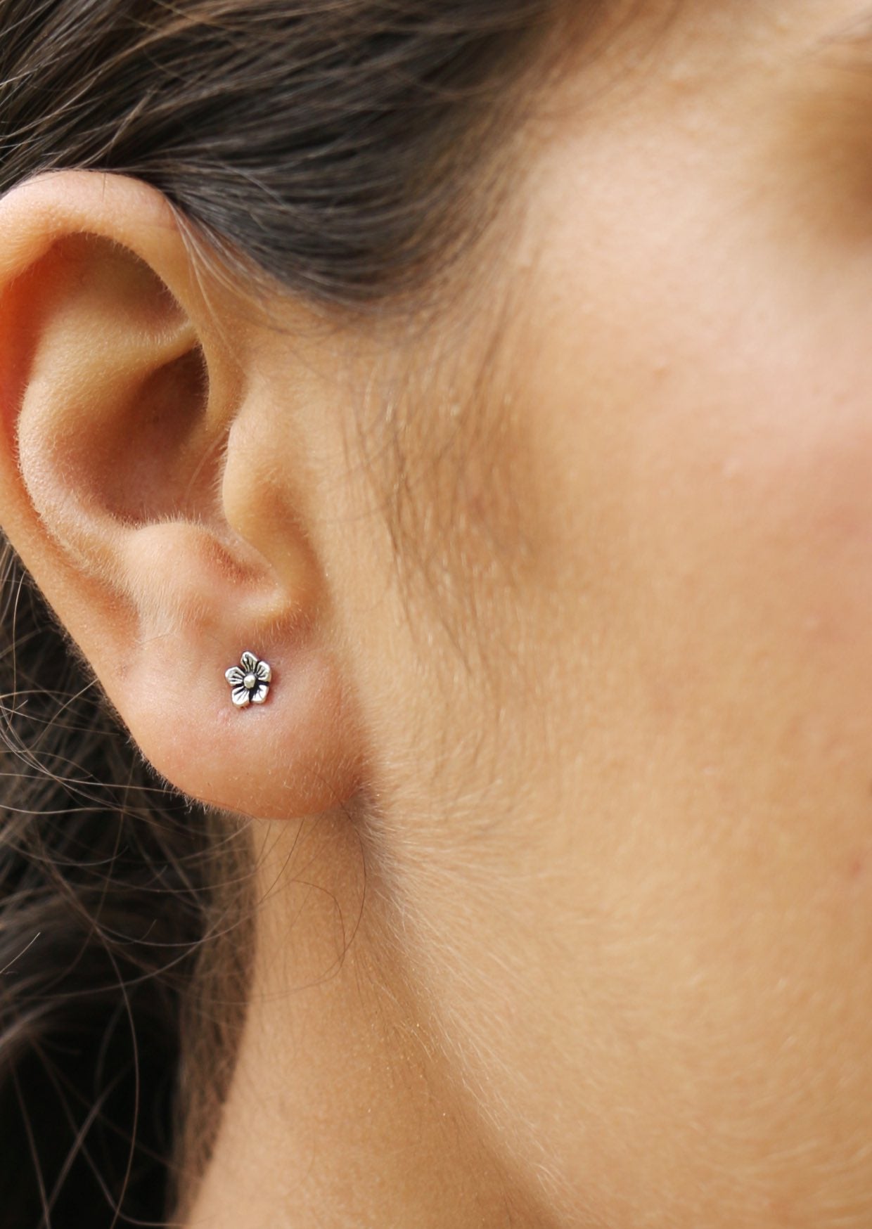 Close up of a woman's ear wearing delicate sterling silver buttercup studs with floral design