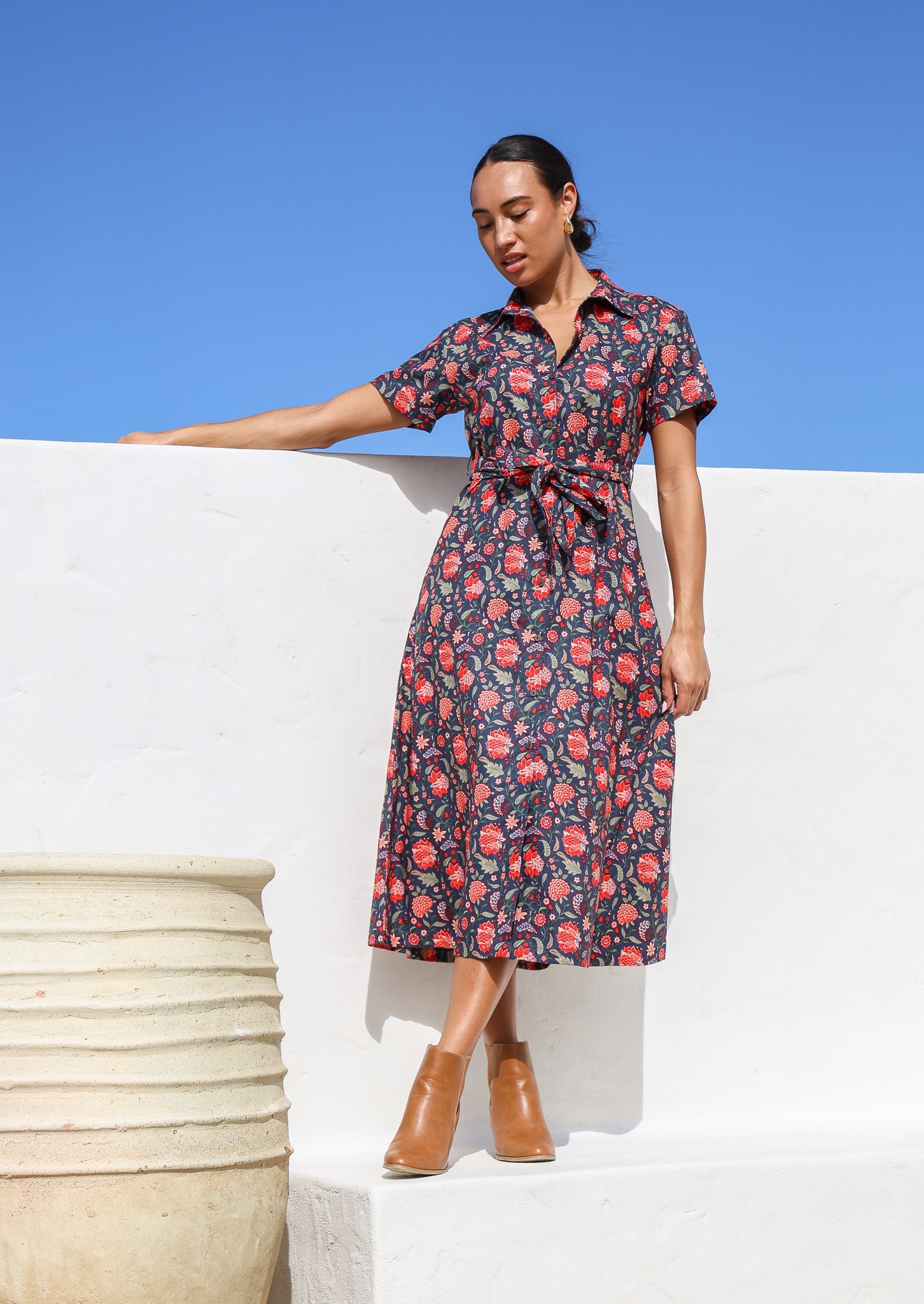 Model stands in sun wearing a short sleeve, button through cotton dress with collar and detachable thick waist tie