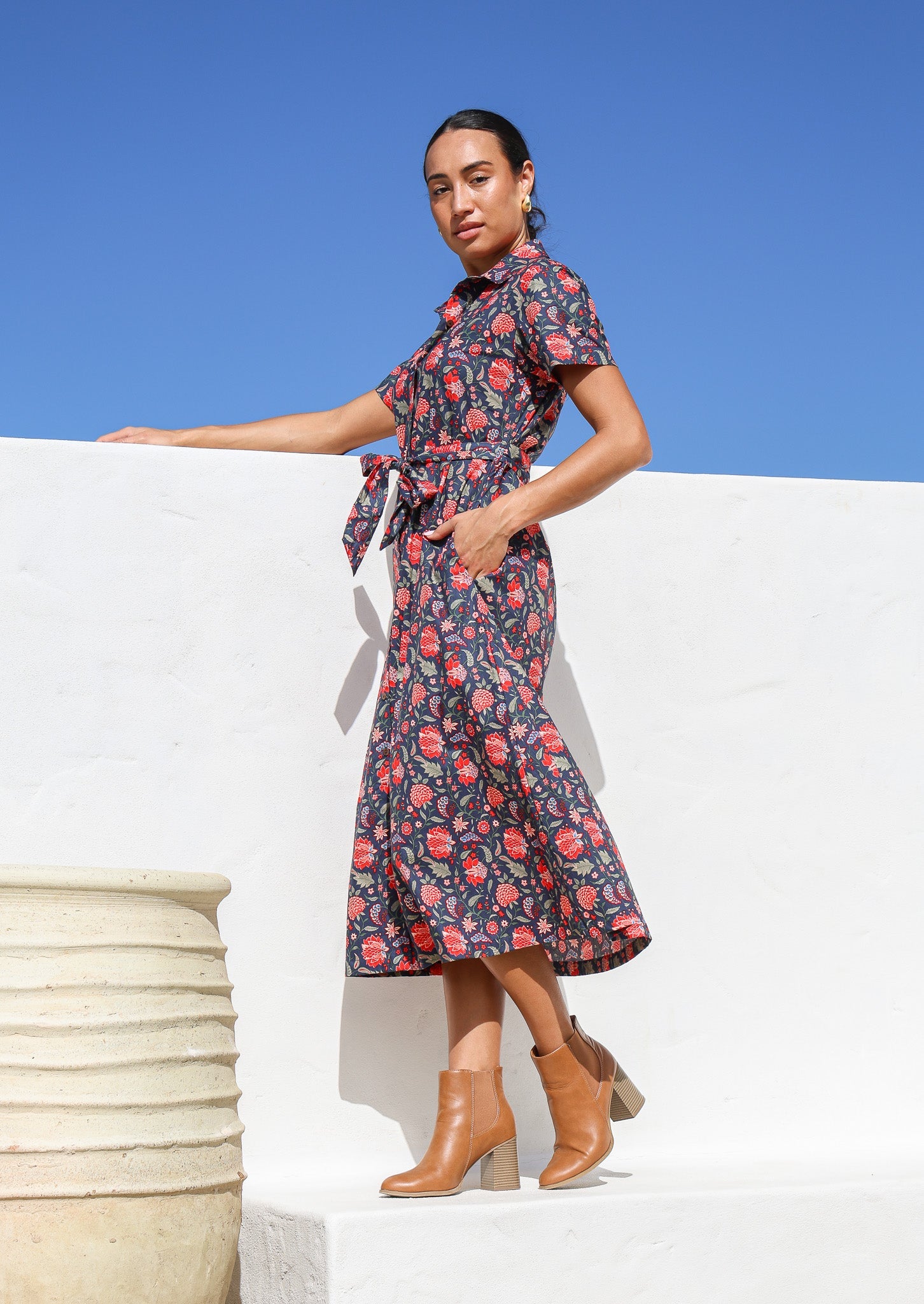 Woman poses in floral printed, 100%  cotton shirt dress with short sleeves and collar, with her hand in side pocket.
