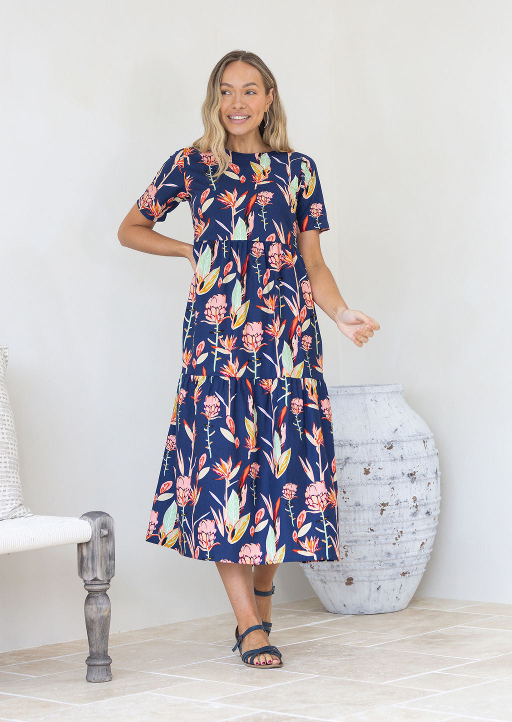 Model wearing short sleeved pink and green floral print navy cotton dress with pockets and round neckline.