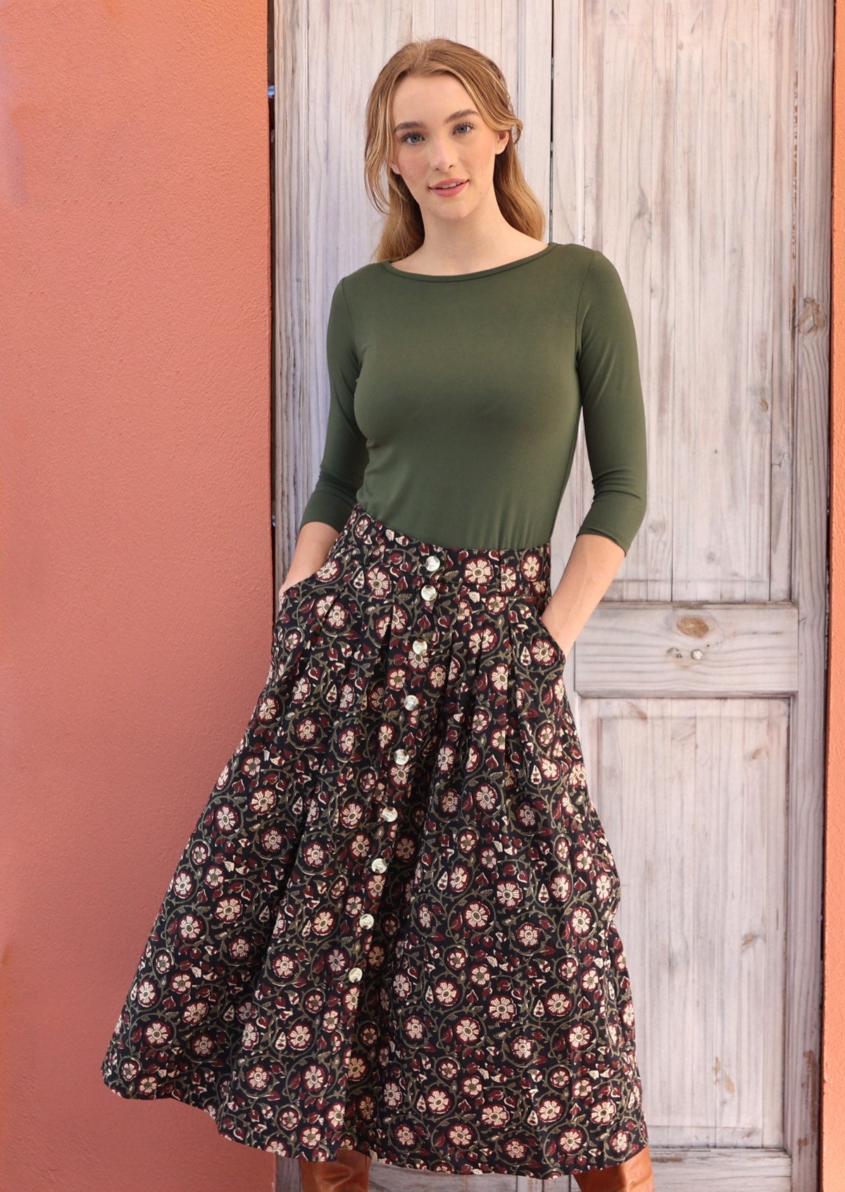 Woman wears black based white and maroon floral print cotton button through skirt with hands in pockets