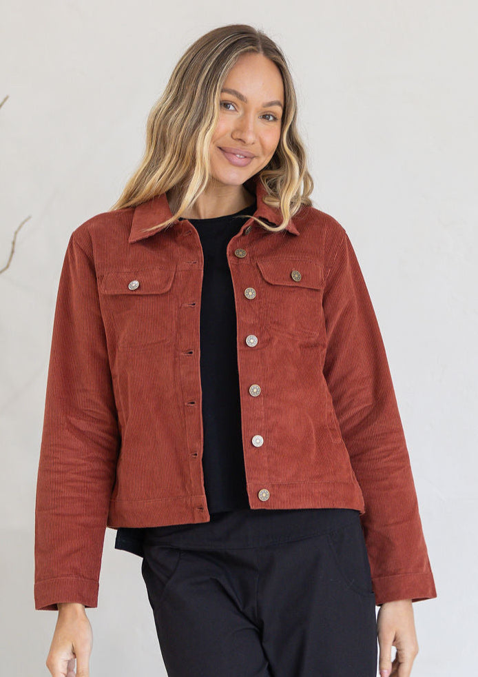 Woman wearing a rust-colored jacket standing against a white wall.