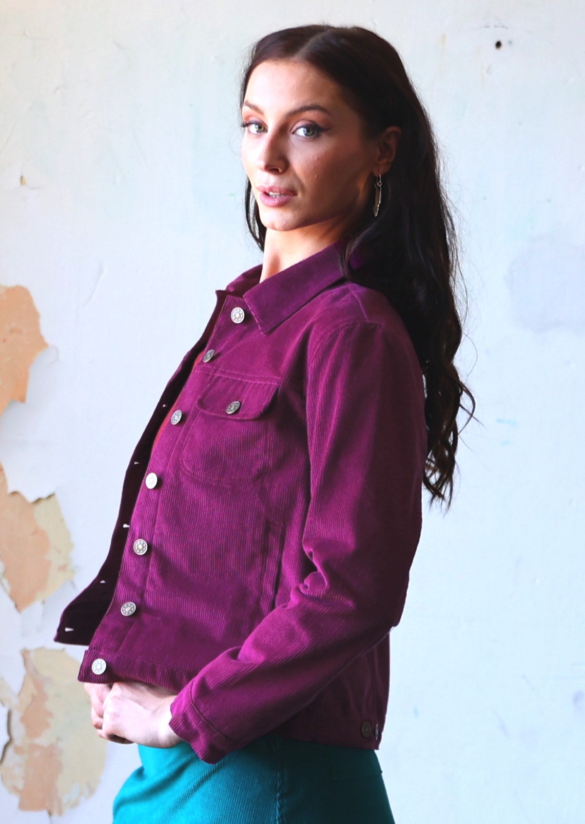 Woman wearing collared purple corduroy jacket with breast and front pockets, and brass buttons