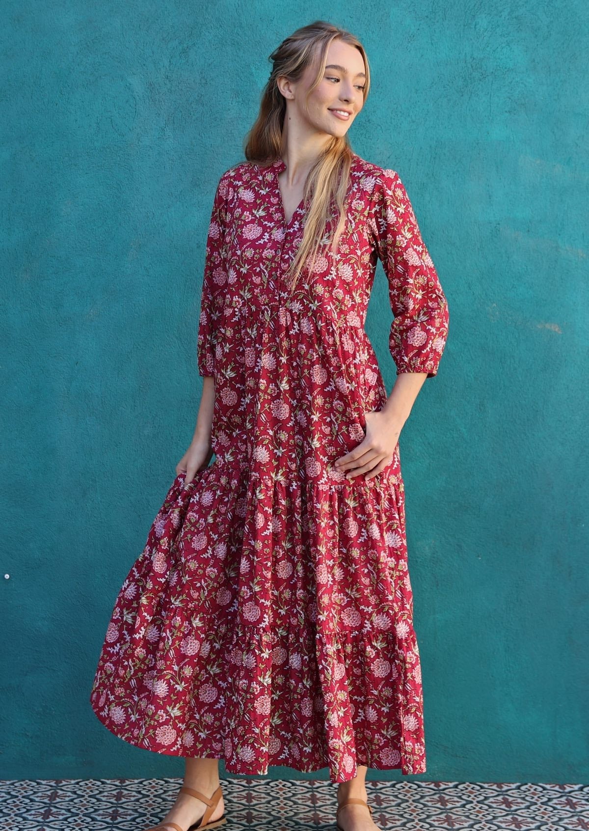 Model poses in floral cotton relaxed fit tiered maxi dress with 3/4 sleeves and buttoned bodice, with thumb hooked in pocket