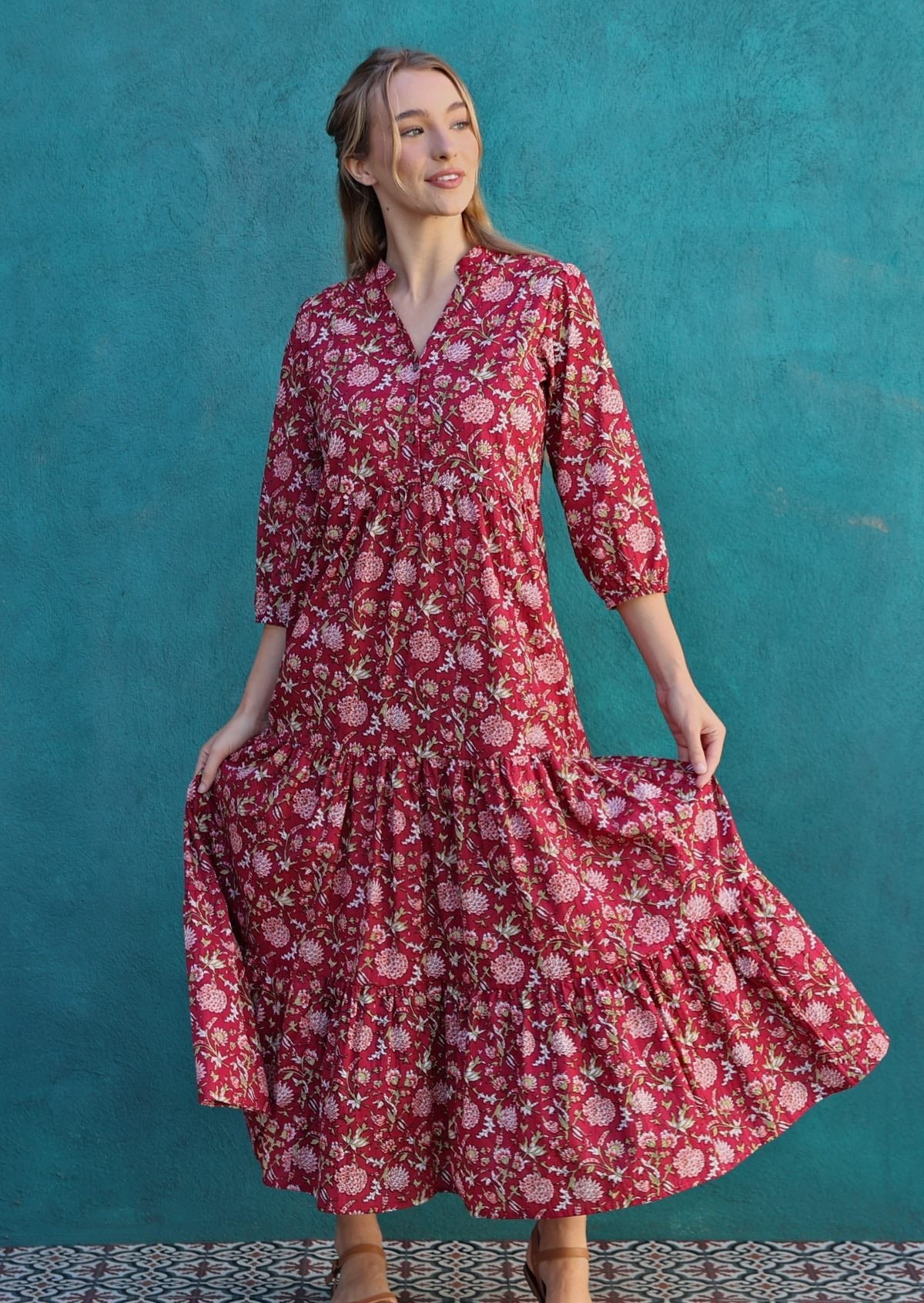 Model poses in deep bright red floral print cotton tiered maxi dress, holding skirt out to show volume