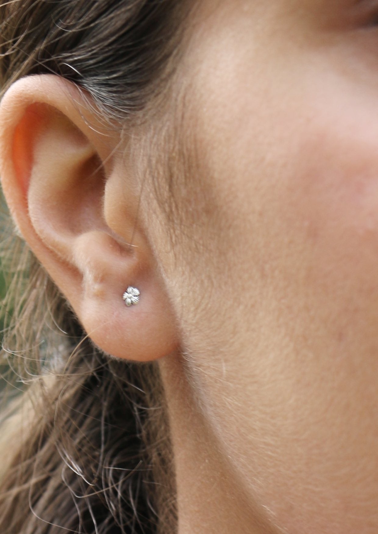 Close-up of an ear wearing a small dainty flower silver studs with soft petals arranged in a bloom