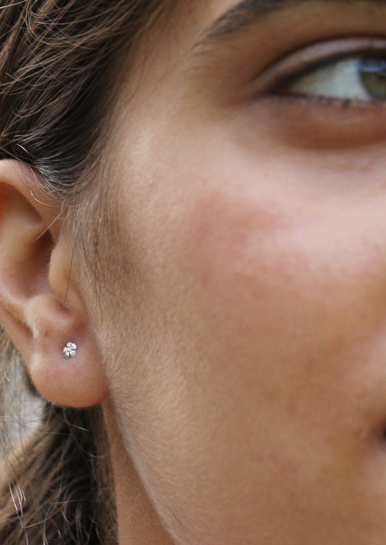 Close up of a person wearing small sterling silver flower studs in bloom, with butterfly backs