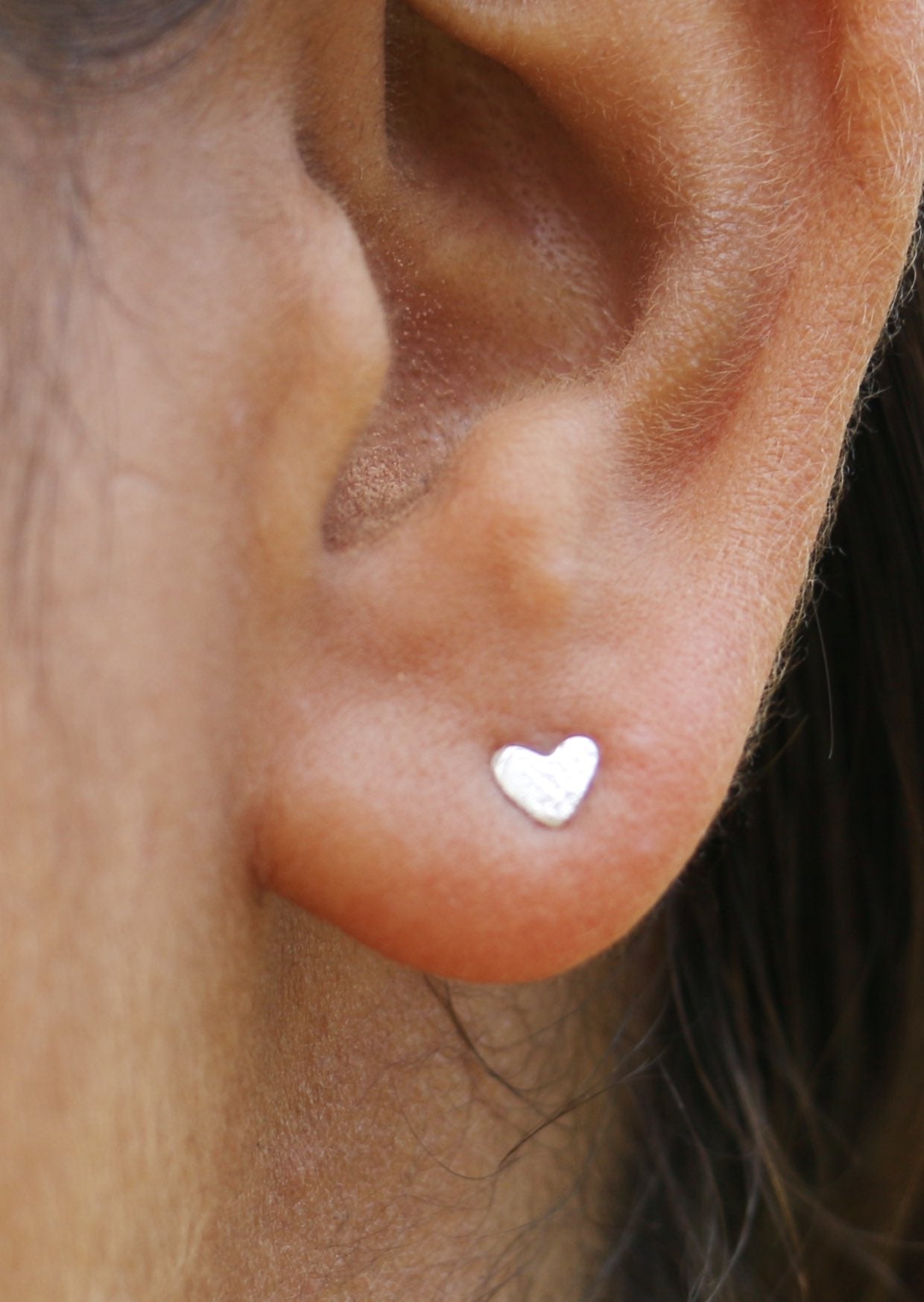 Close-up of an ear wearing delicate sterling silver heart studs with a textured design