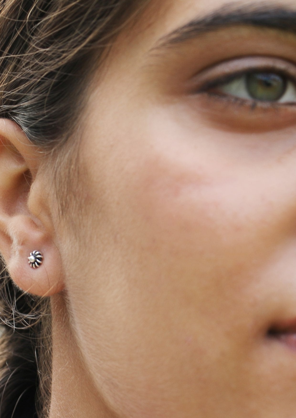 Close-up of a person wearing a small silver dandelion stud earrings with delicate wire spring petals