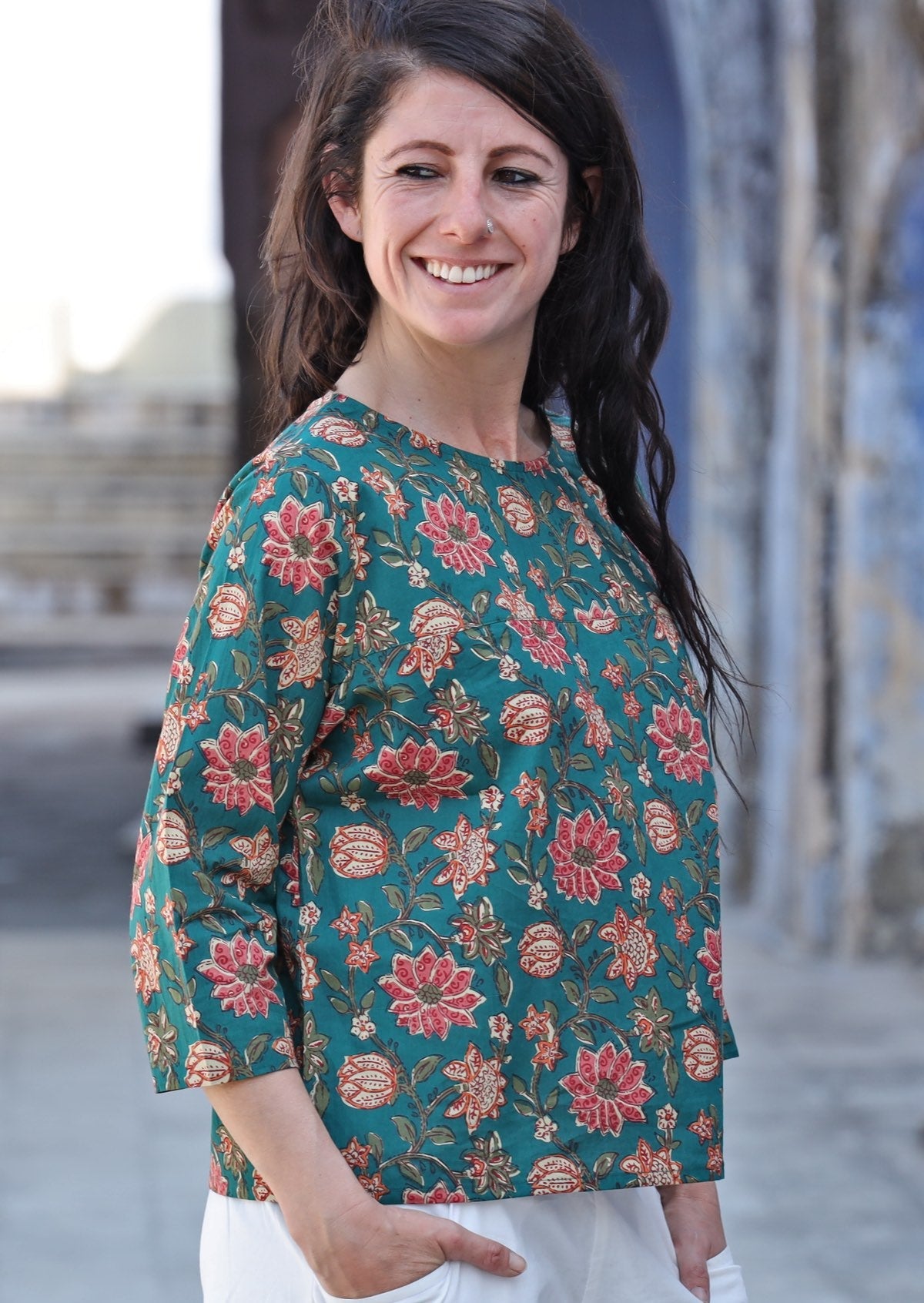Woman smiling over her shoulder wearing relaxed fit cotton top with 3/4 sleeves and round neckline in green with a floral print