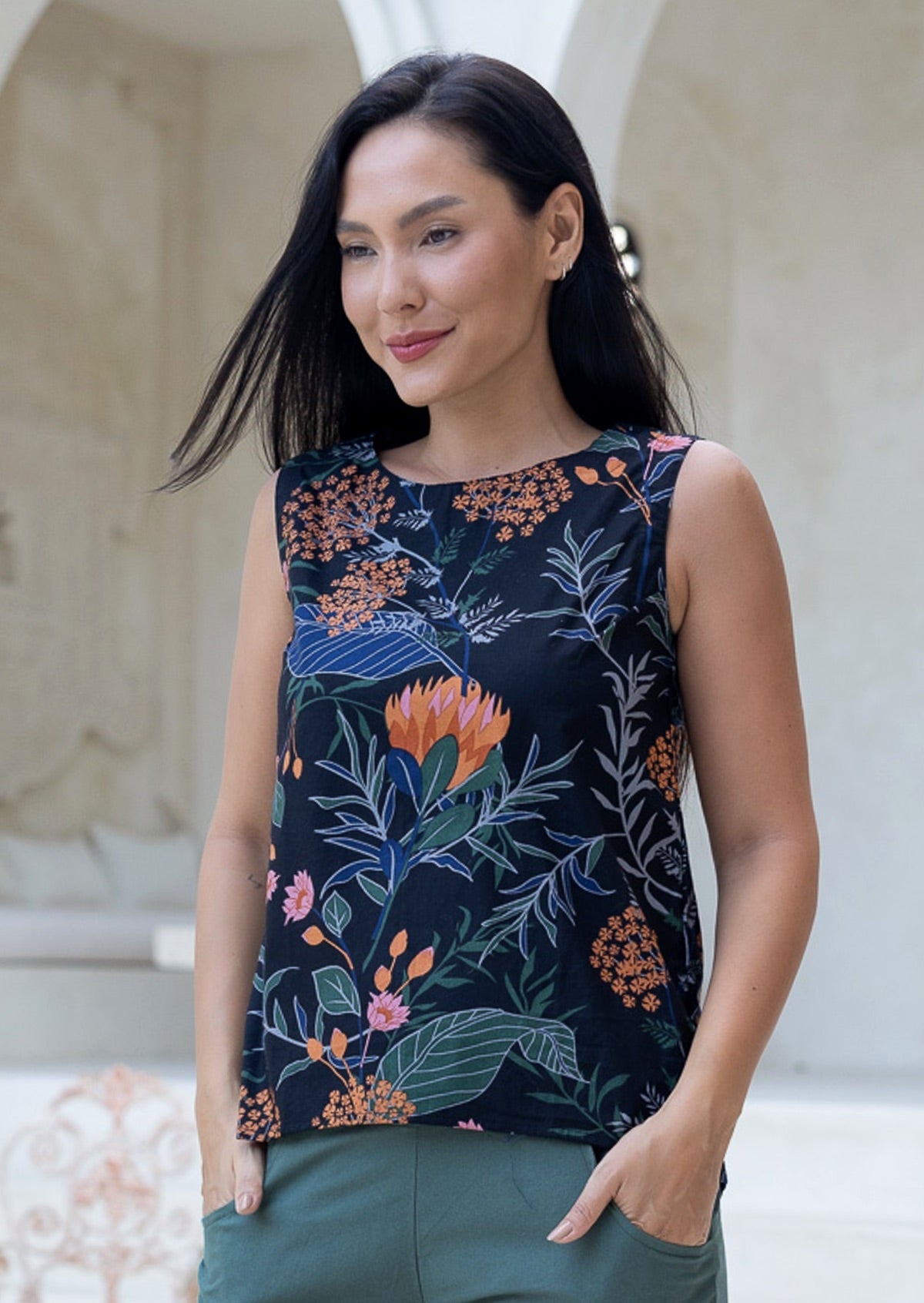 Model posing in a 100% cotton sleeveless top with an A-line cut and round neckline, featuring a dark base with pink and orange floral with green and blue leafy prints