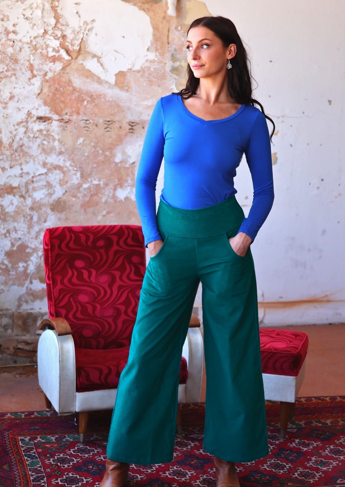 Model poses in wide leg teal coloured corduroy pants with hands in deep pockets, paired with an electric blue long sleeve top